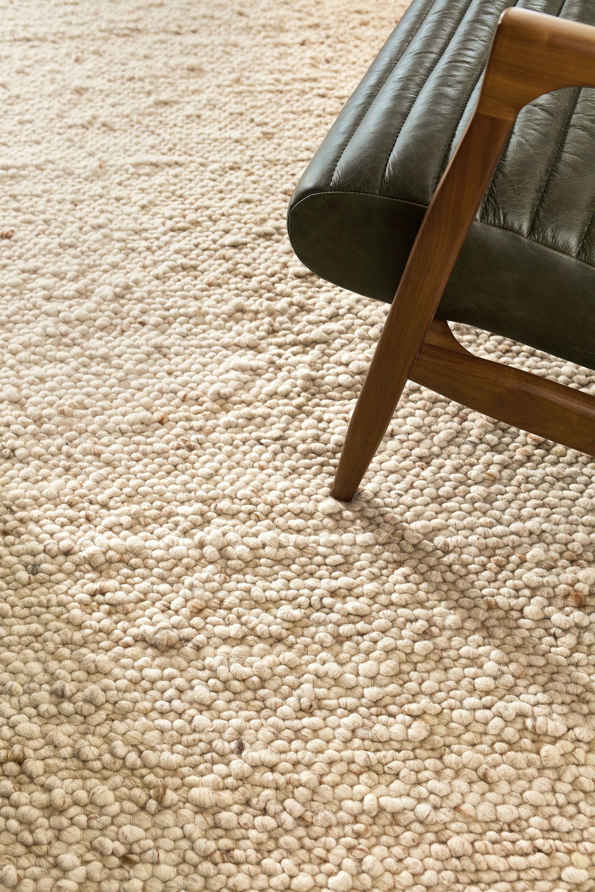 Detail of cobble 8 by 10 rug in ecru and callan chair in palermo olive with walnut legs.