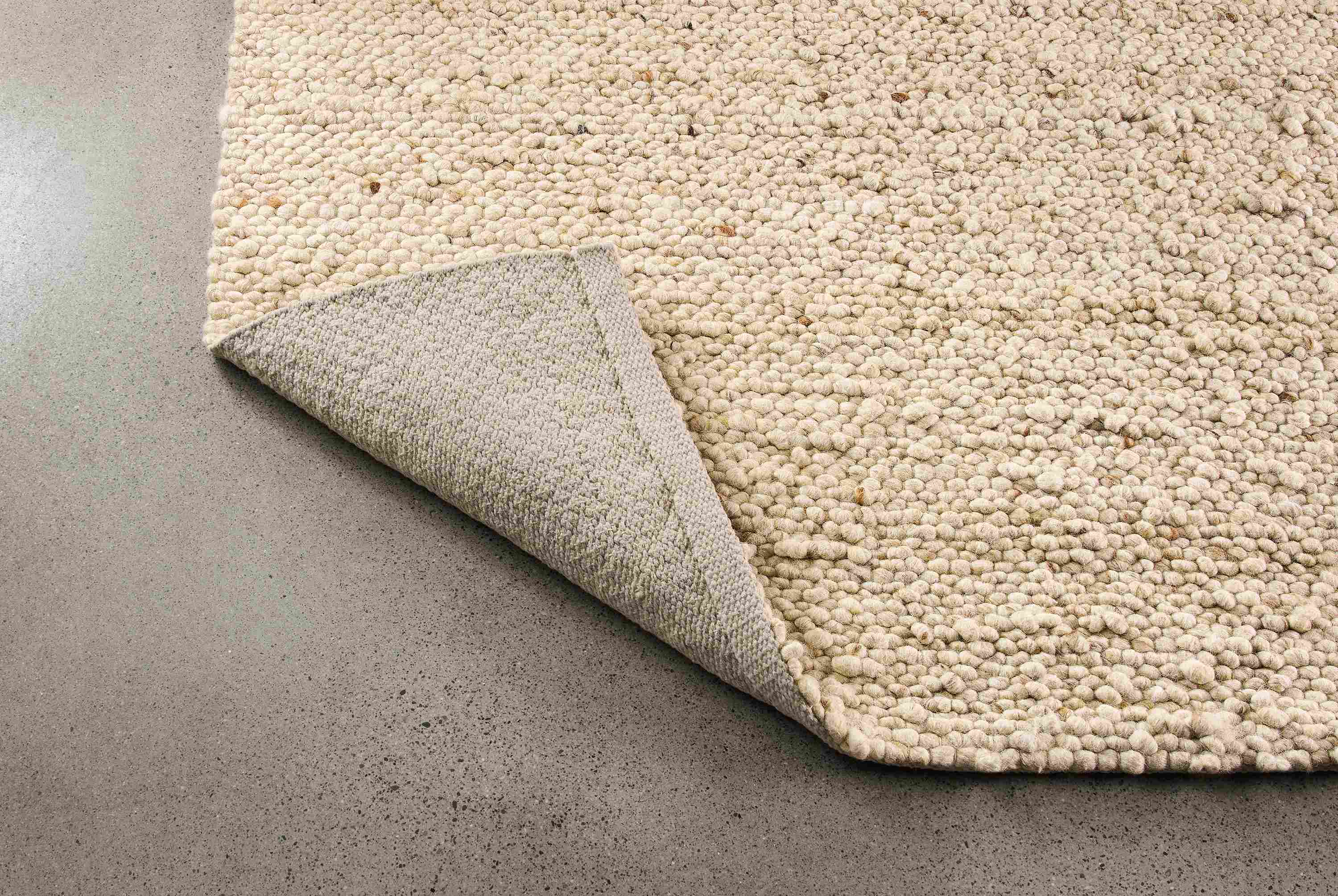 Cobble 8 by 10 rug in ecru shown with corner flipped up to show underside of rug.
