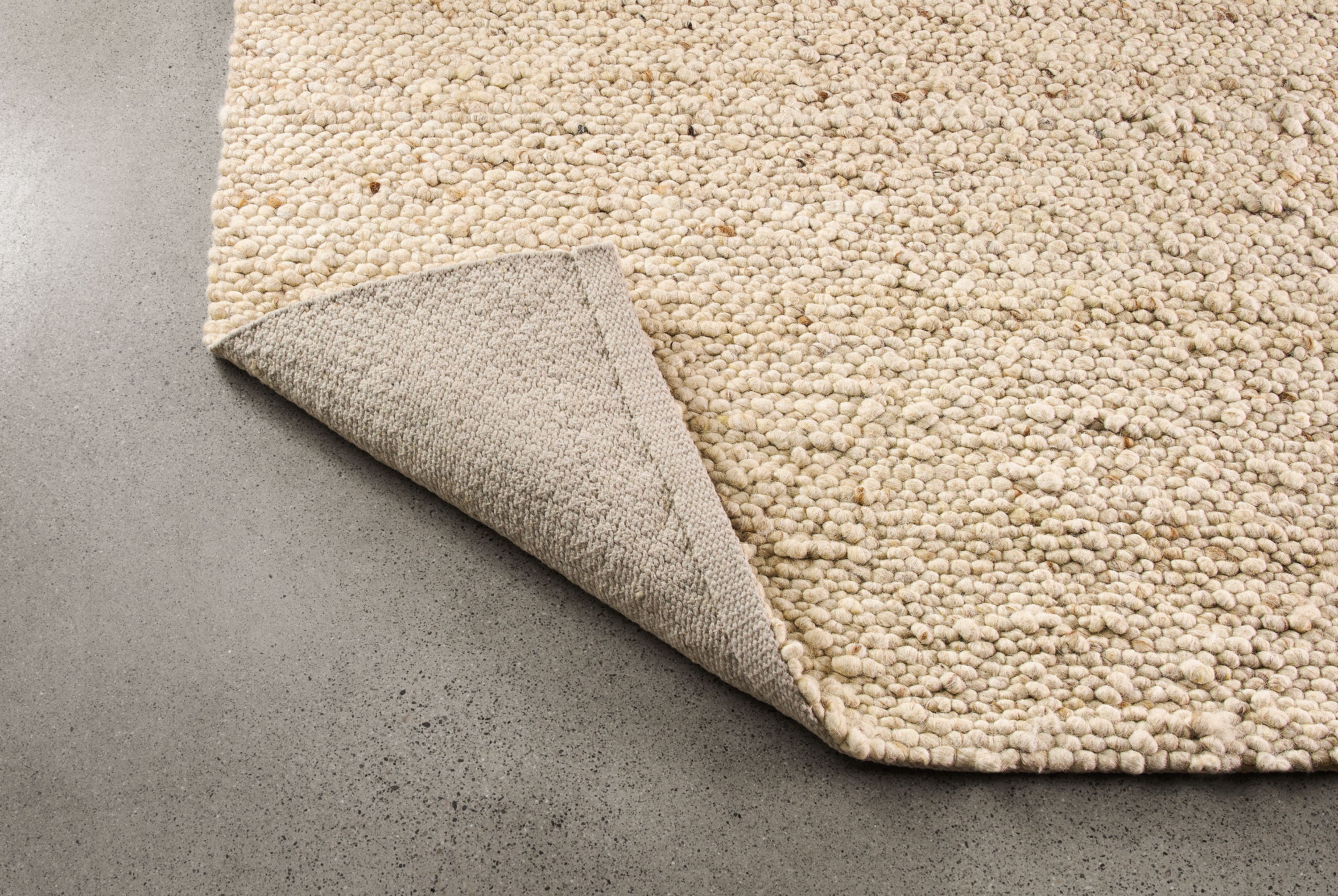 Cobble 8 by 10 rug in ecru shown with corner flipped up to show underside of rug.