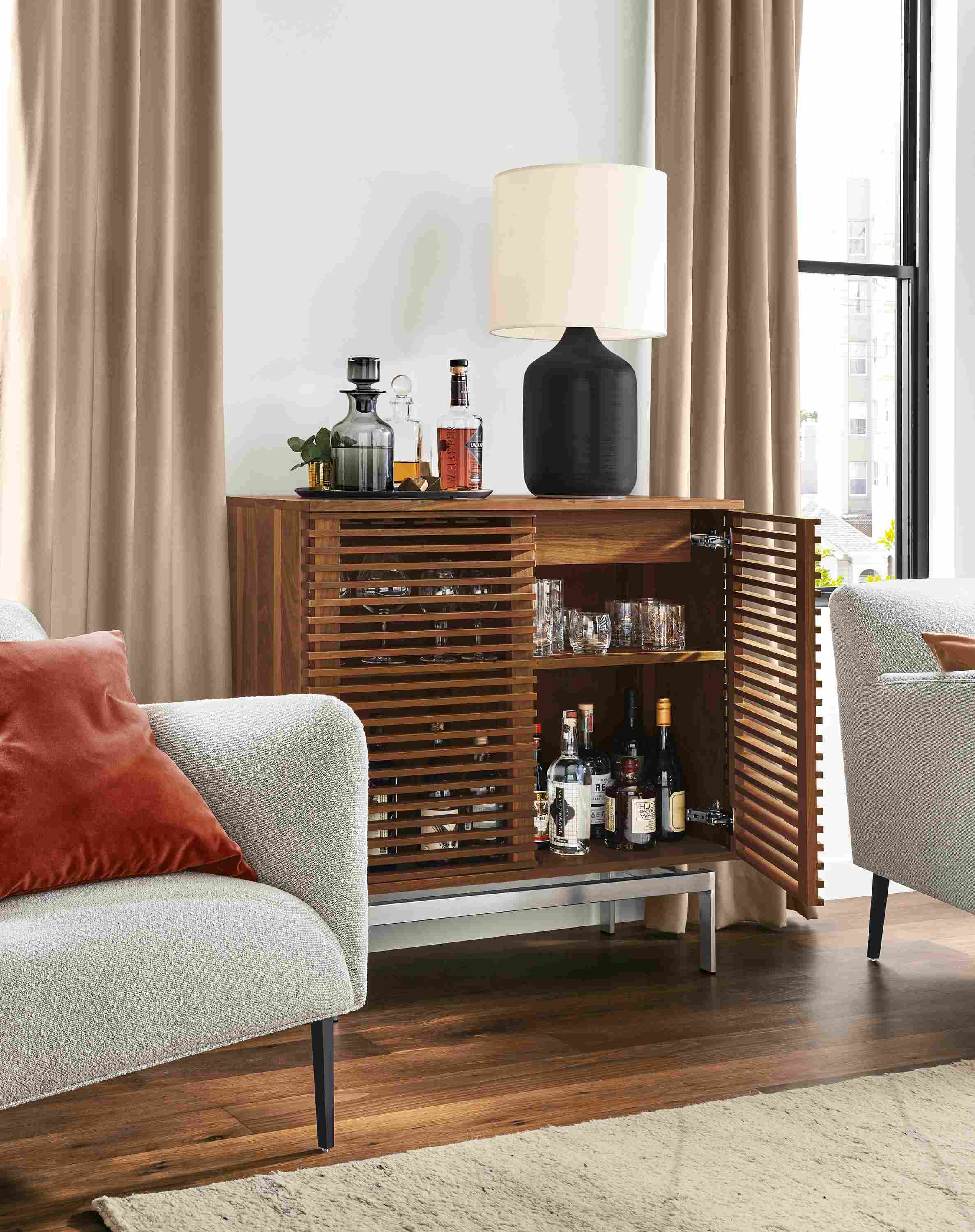 Detail of Coles two-door bar cabinet in walnut with stainless steel base in living room with right door open.