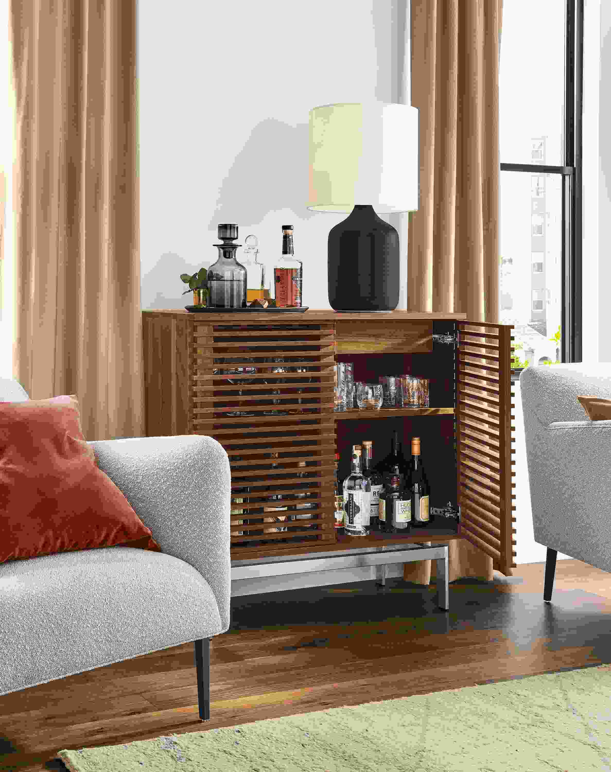 Detail of Coles two-door bar cabinet in walnut with stainless steel base in living room with right door open.