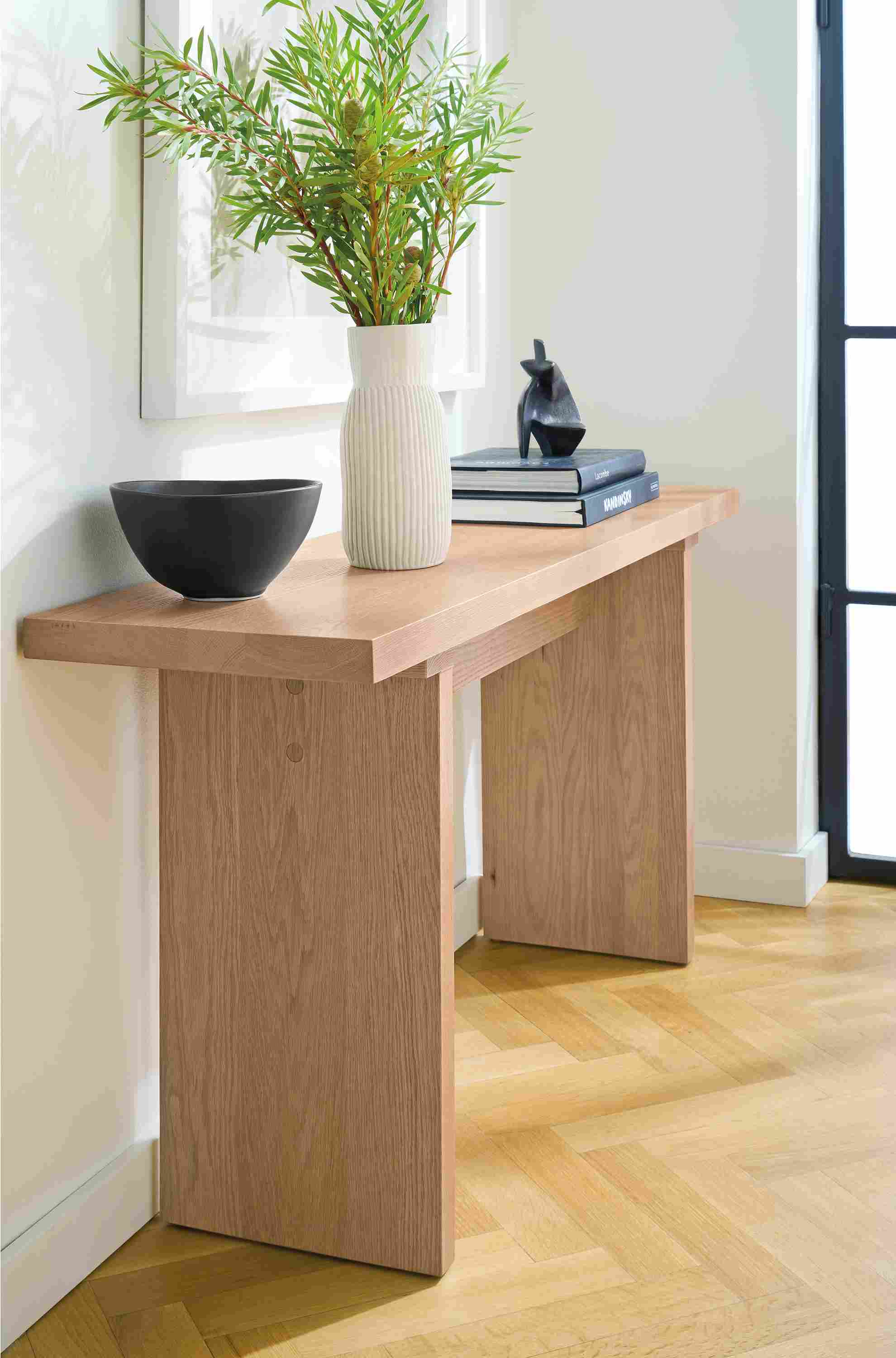 Room corner with Corbett 60-wide console table in rye on red oak and Anya large serving bowl in black.