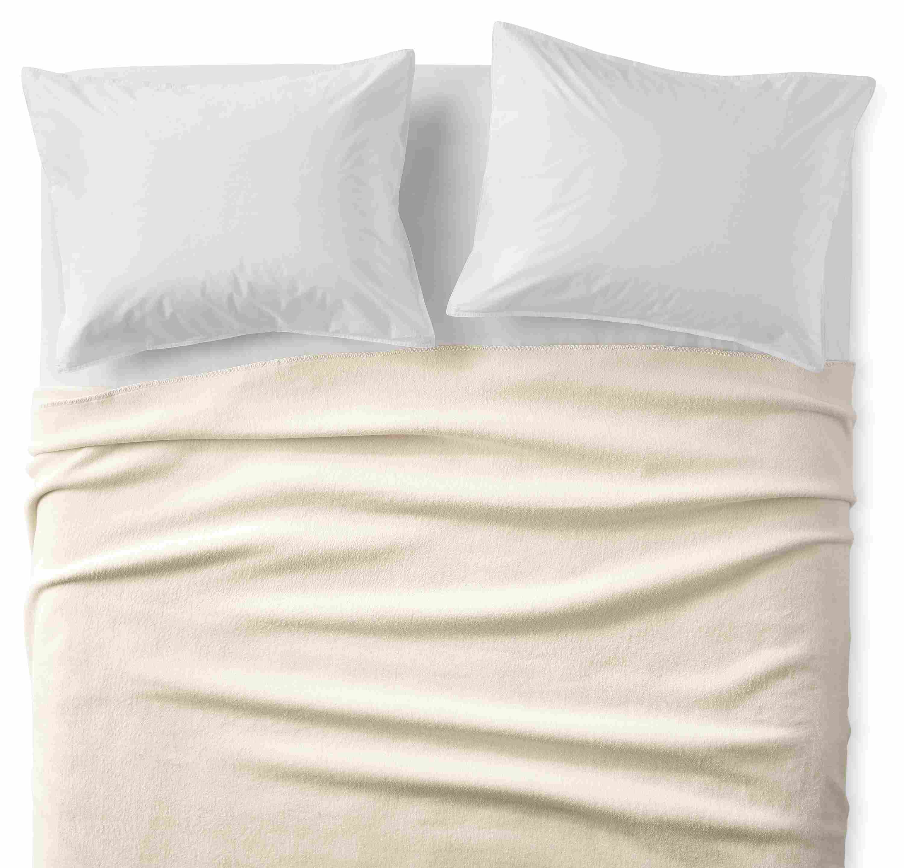 Overhead view of a cotton fleece full/queen blanket in ivory on a bed with white sheets and pillows.