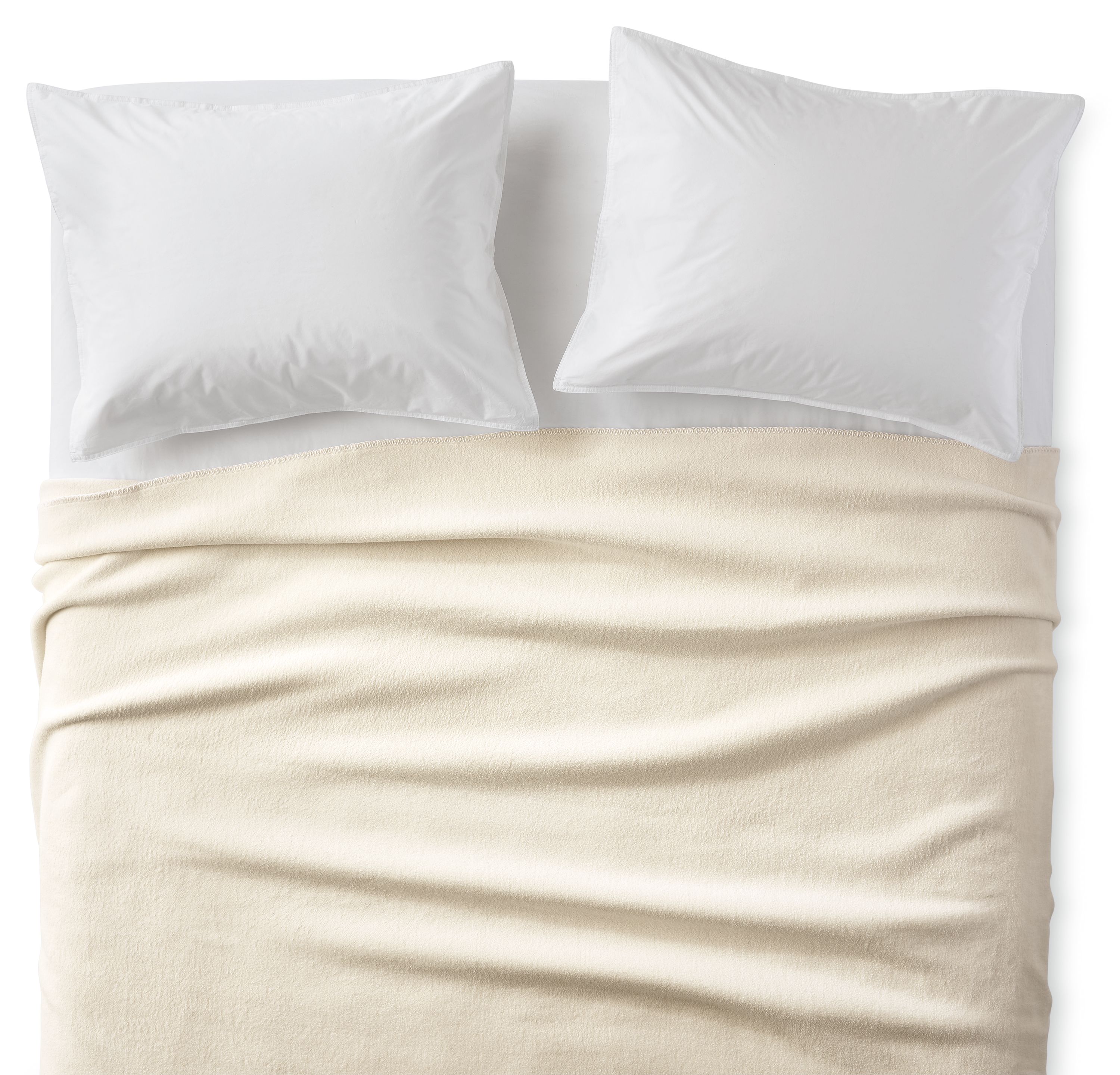 Overhead view of a cotton fleece full/queen blanket in ivory on a bed with white sheets and pillows.