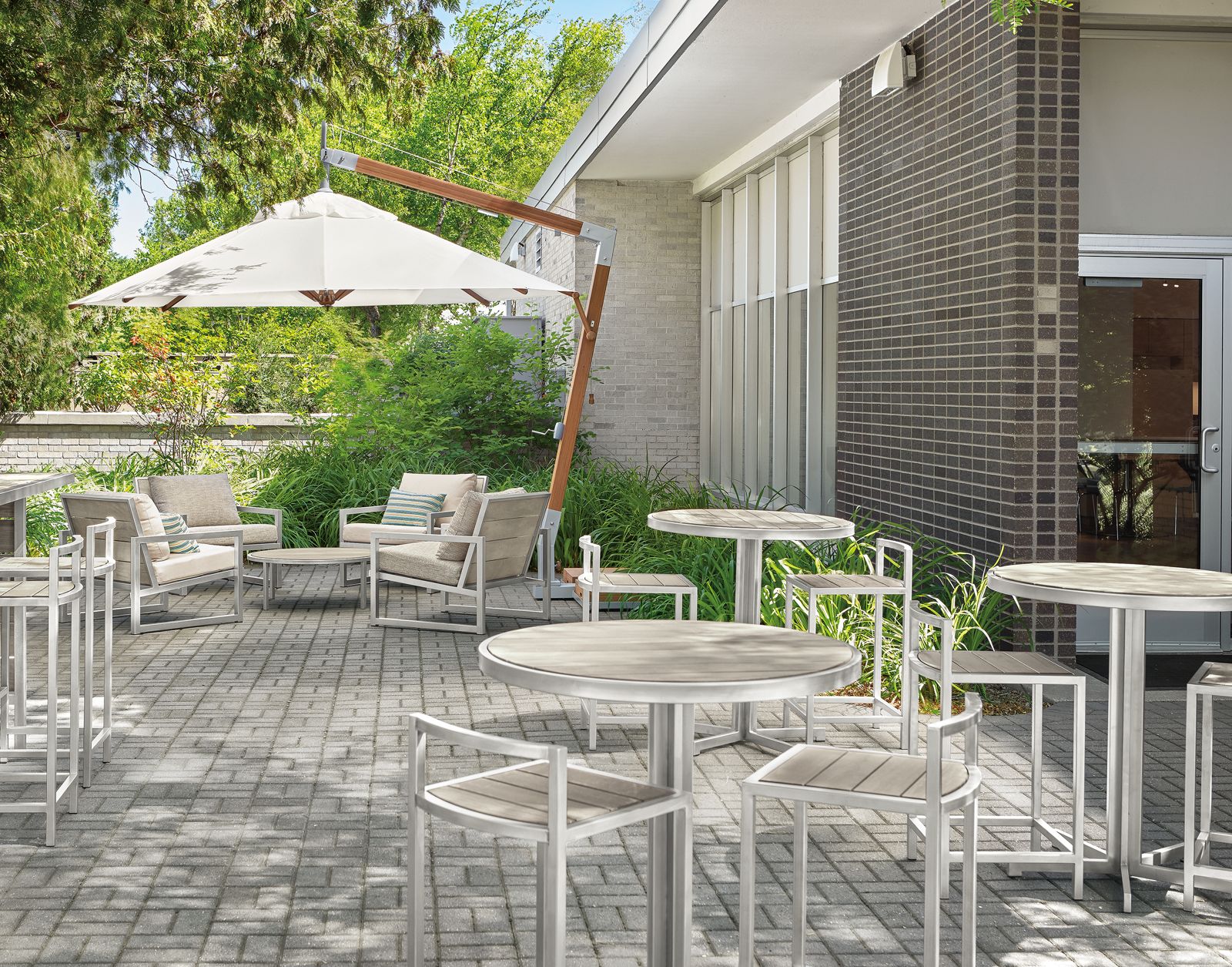 outdoor dining area with cumulo patio umbrella, montego chairs, tables, stools and bar  in aged ash.