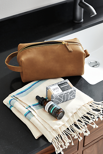 detail of leather dopp kit next to folded towel with soap and beard oil.