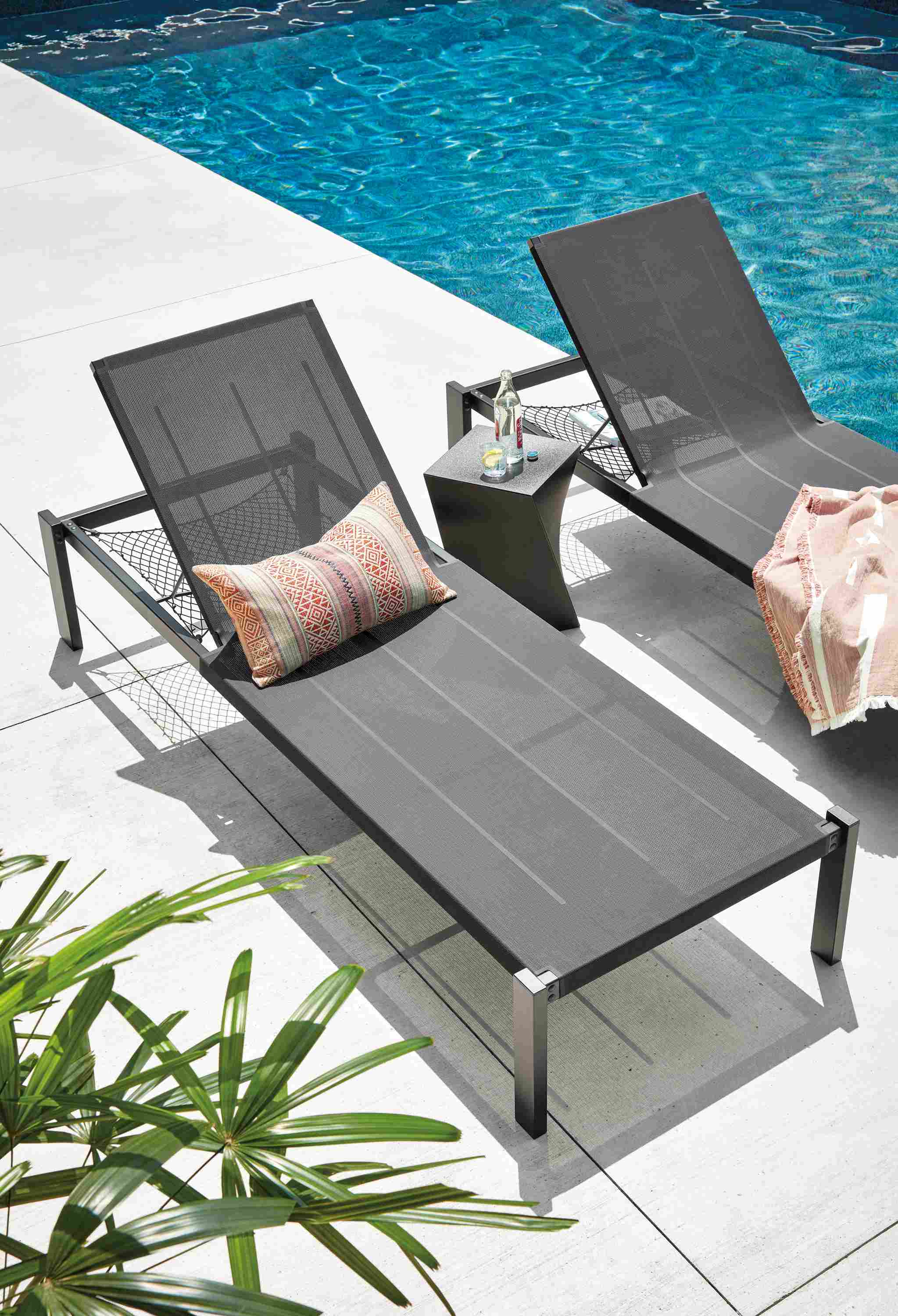 High-angle image of 2 Dorian chaises with storage net in black with a Kubik stool in black near a pool.