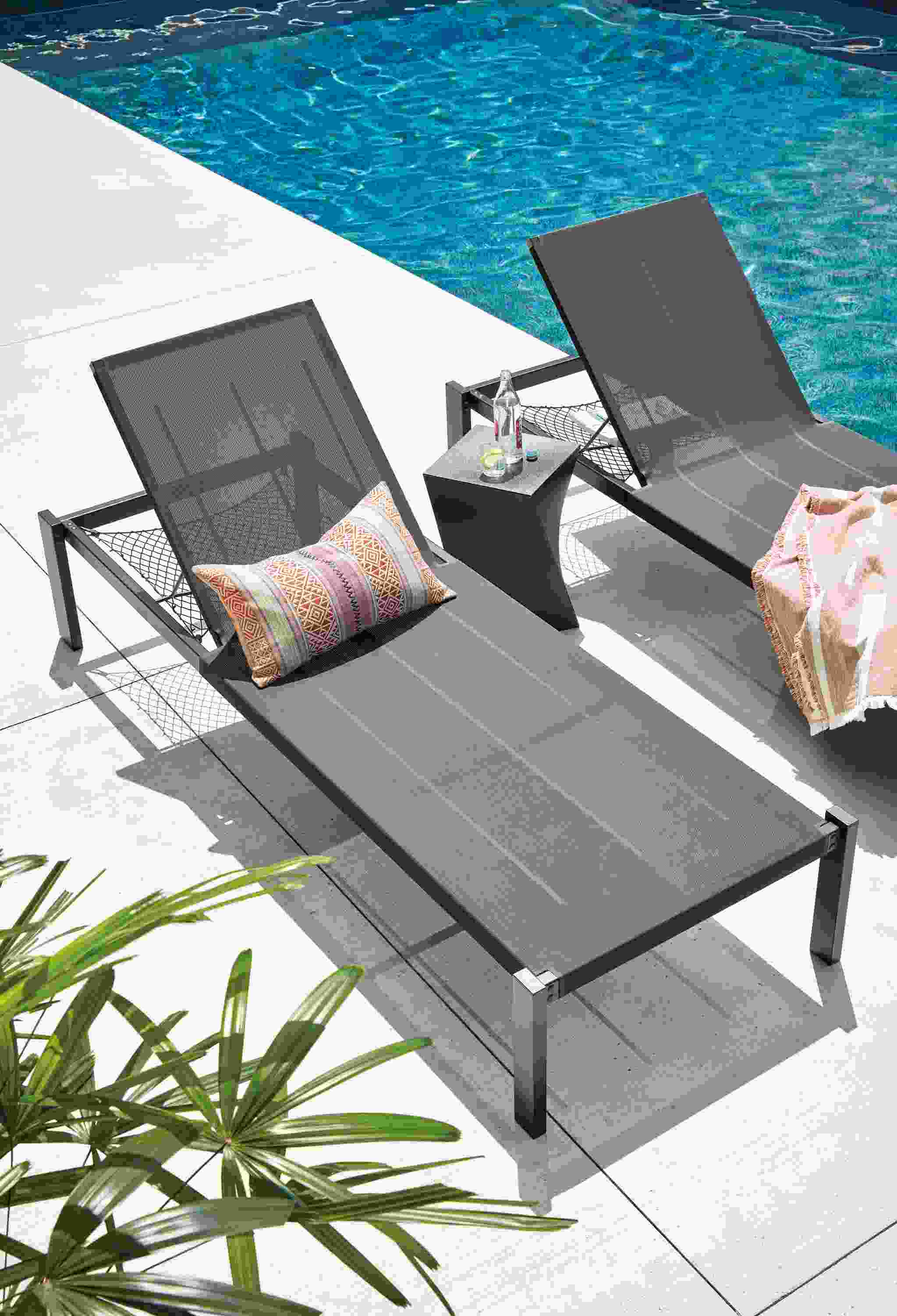 High-angle image of 2 Dorian chaises with storage net in black with a Kubik stool in black near a pool.