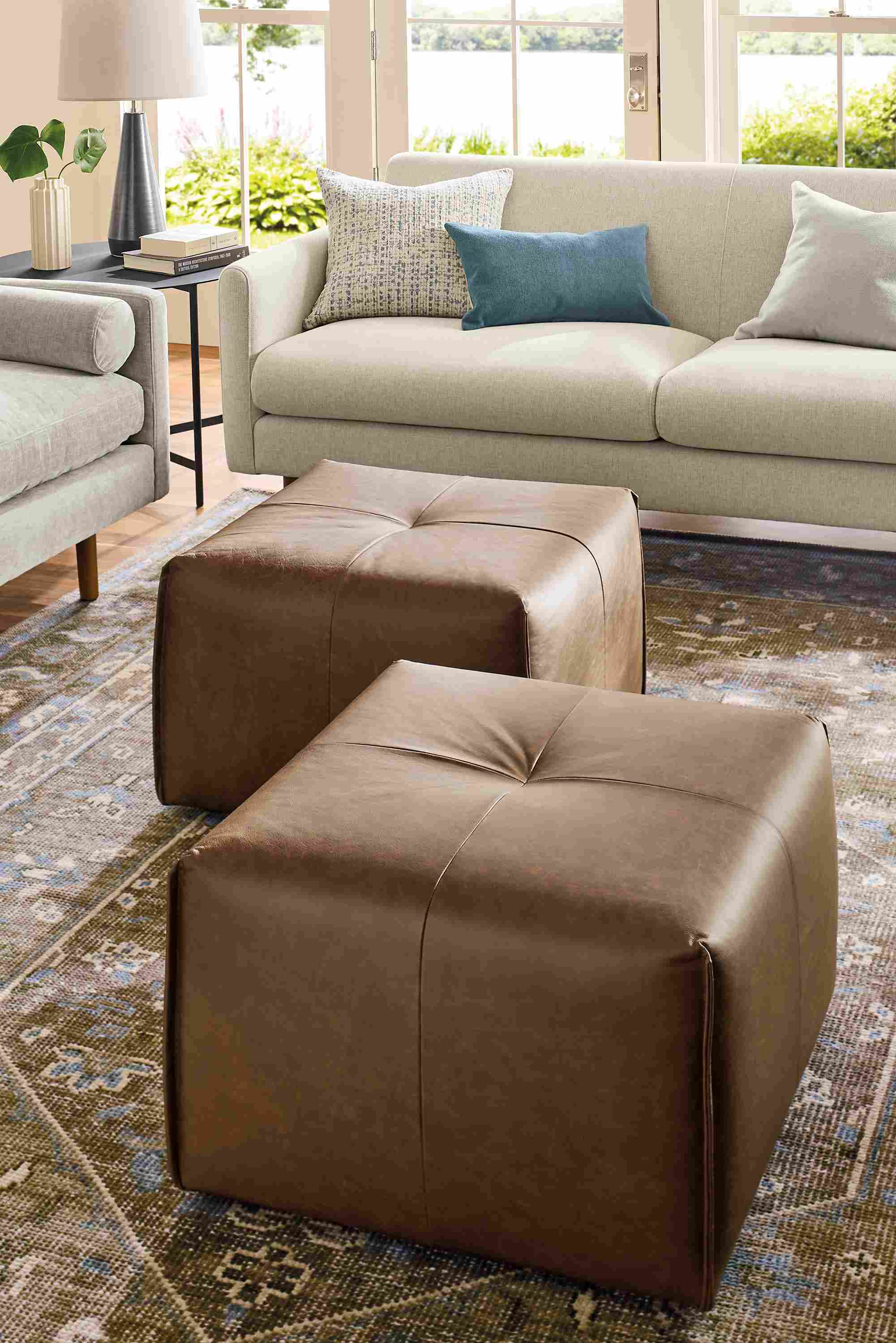 Living room with 2 dupree ottomans in palermo bourbon leather, vienna sofa in sumner linen and veda rug in moss.