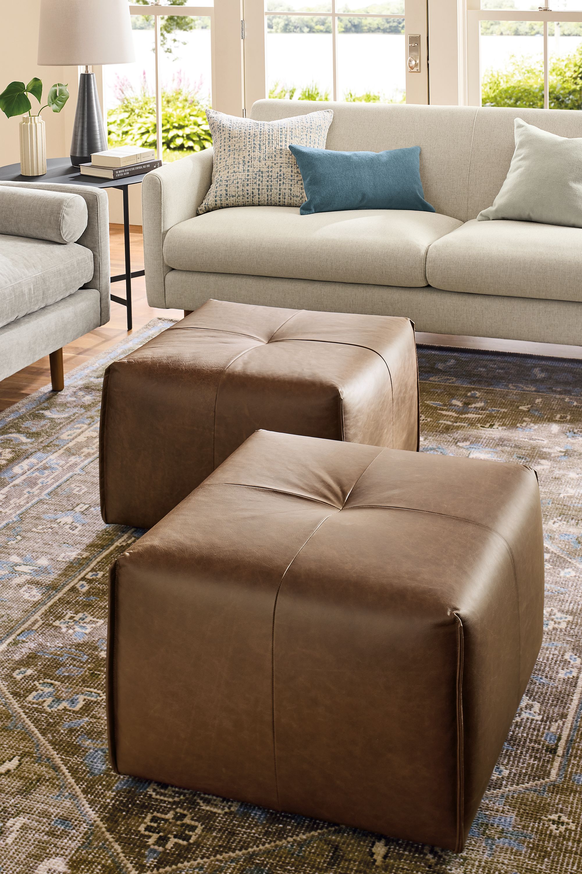 Living room with 2 dupree ottomans in palermo bourbon leather, vienna sofa in sumner linen and veda rug in moss.