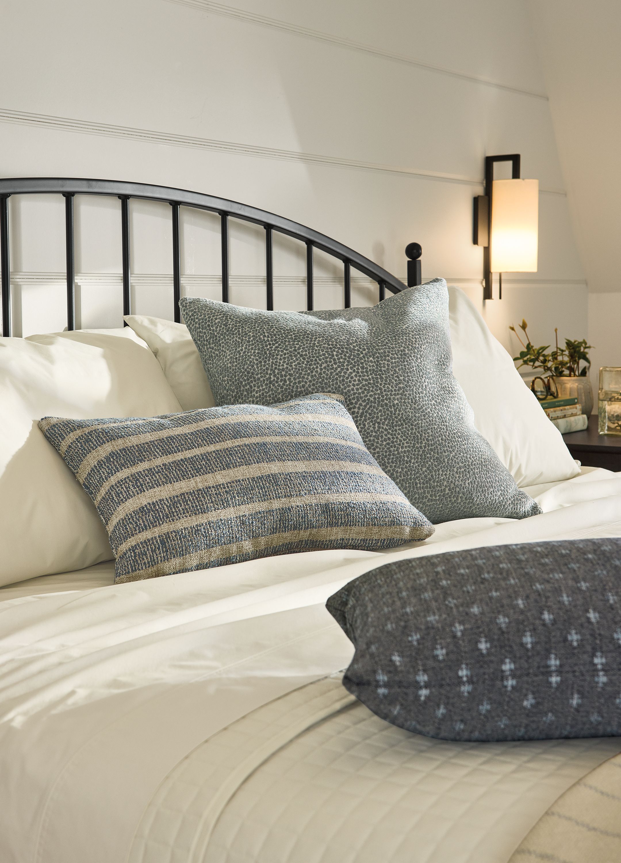 Detail of knife edge throw pillows in auckland denim, faron cadet and lockwood navy on a Joyce king bed in natural steel.