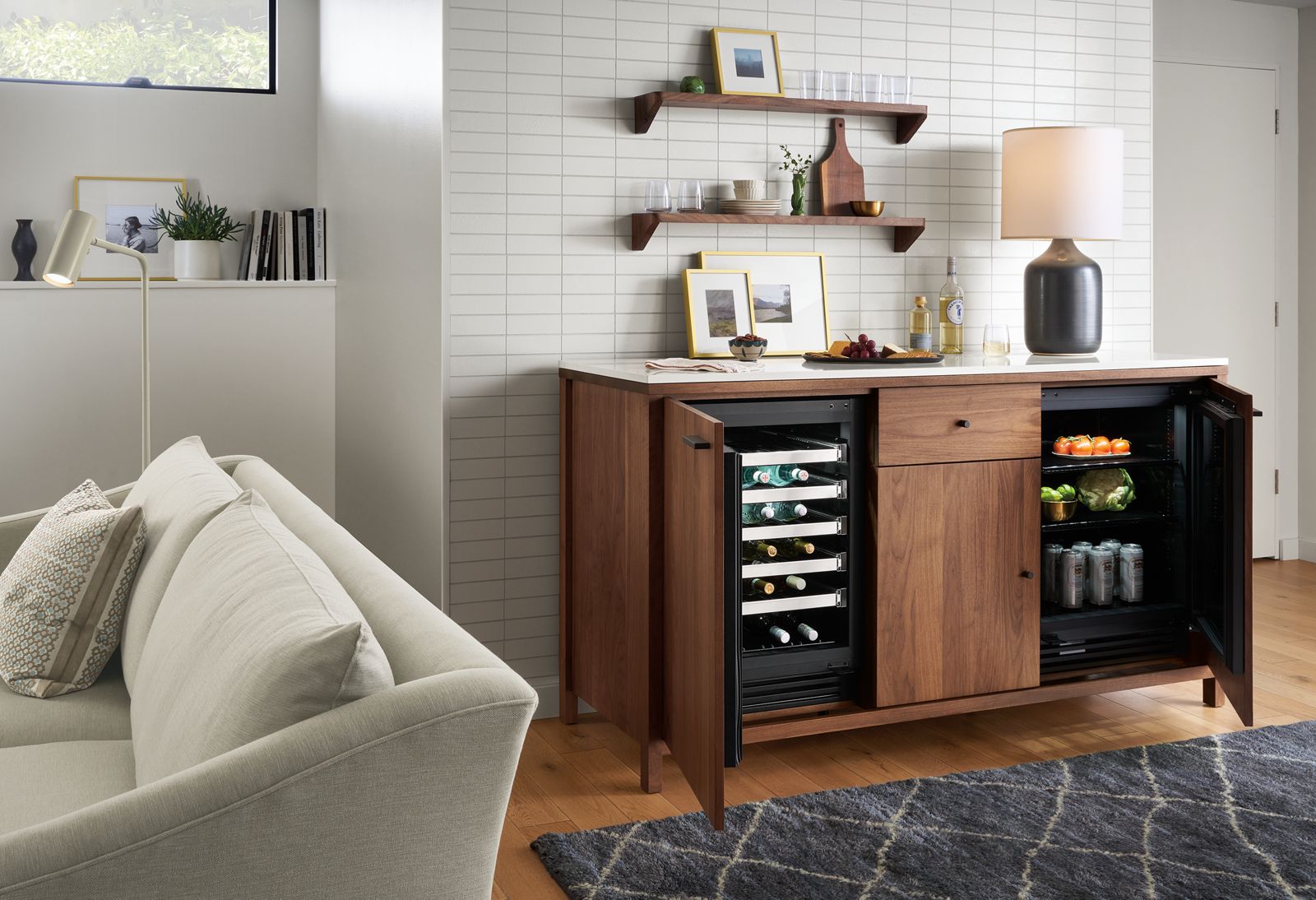 Living room with Emerson 72 wide double fridge cabinet in walnut, showing open wine fridge and 2-shelf fridge, Maeve 93 wide two cushion sofa in Yana Natural and Kalindi 6 x 9 rug in Smoke.