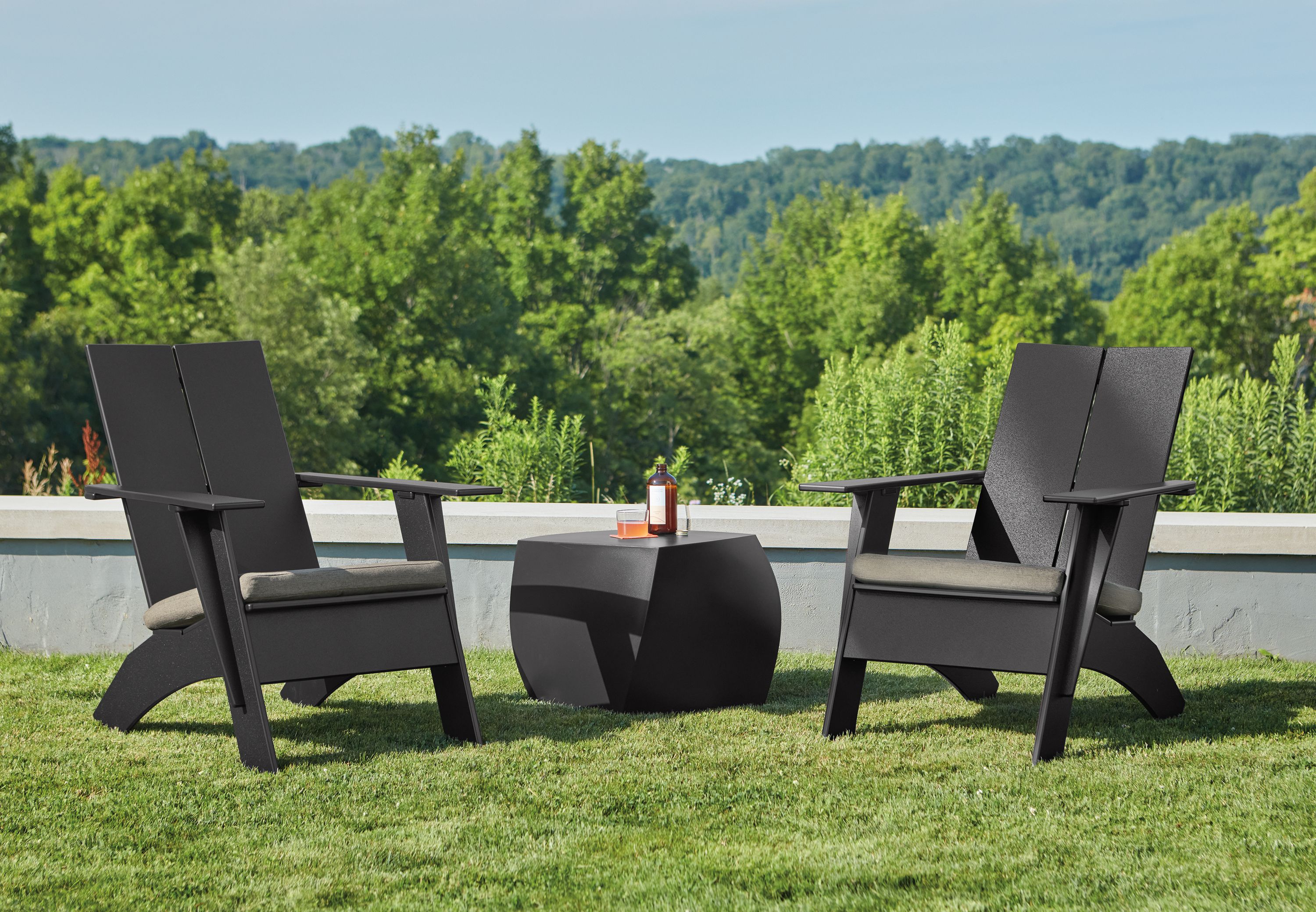 two emmet lounge chairs with cushions flanking a gehry side table on a lawn.