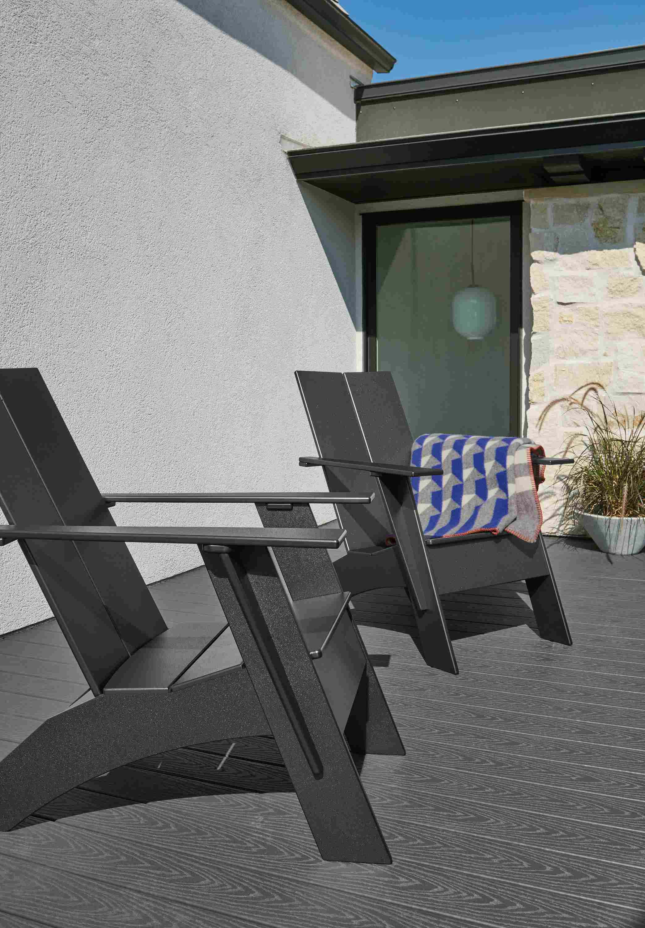 Two outdoor Emmet tall lounge chairs in black with Kvam throw in blue.