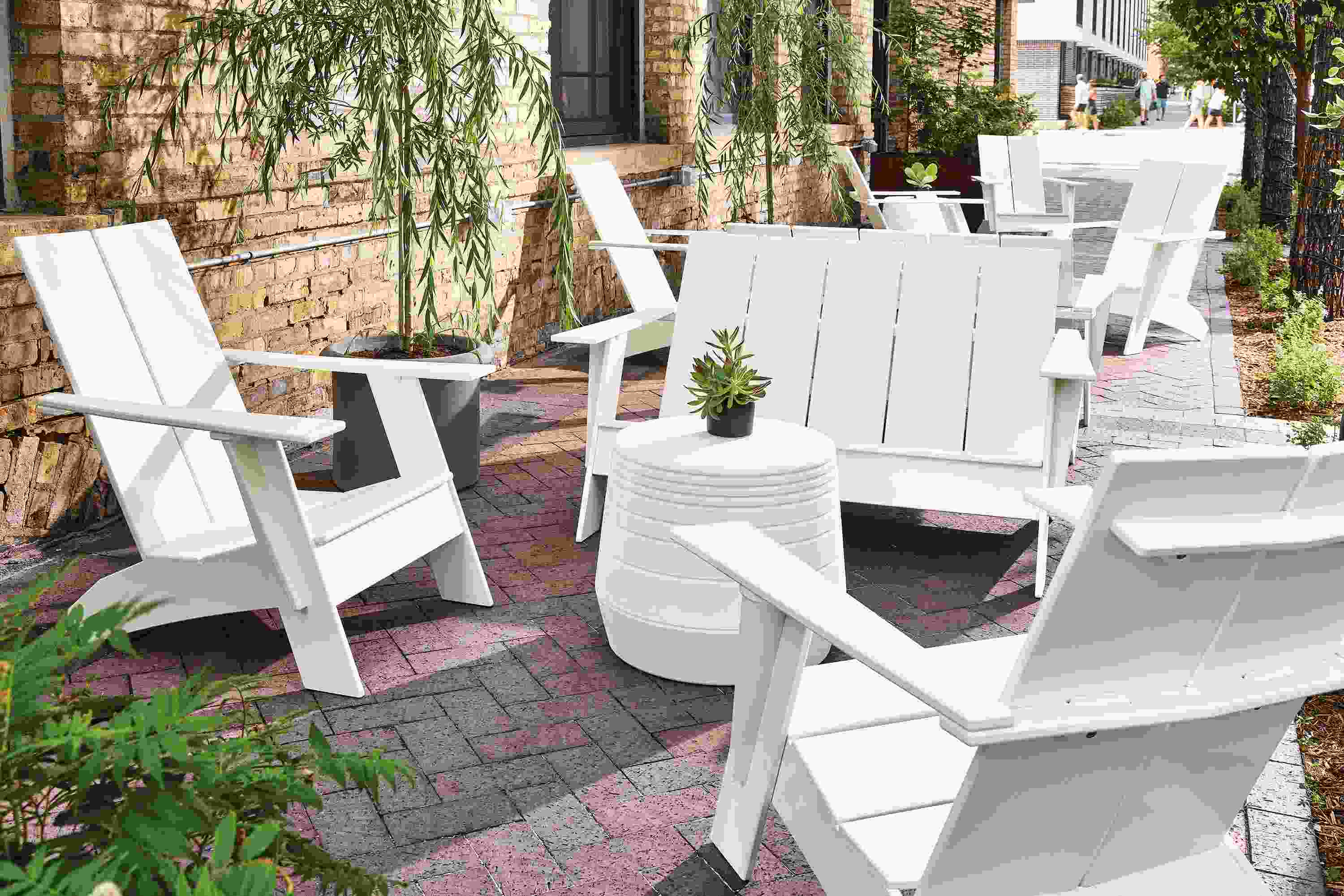 Outdoor brick walkway with several white emmet sofas and chairs and a cusp stool in white.