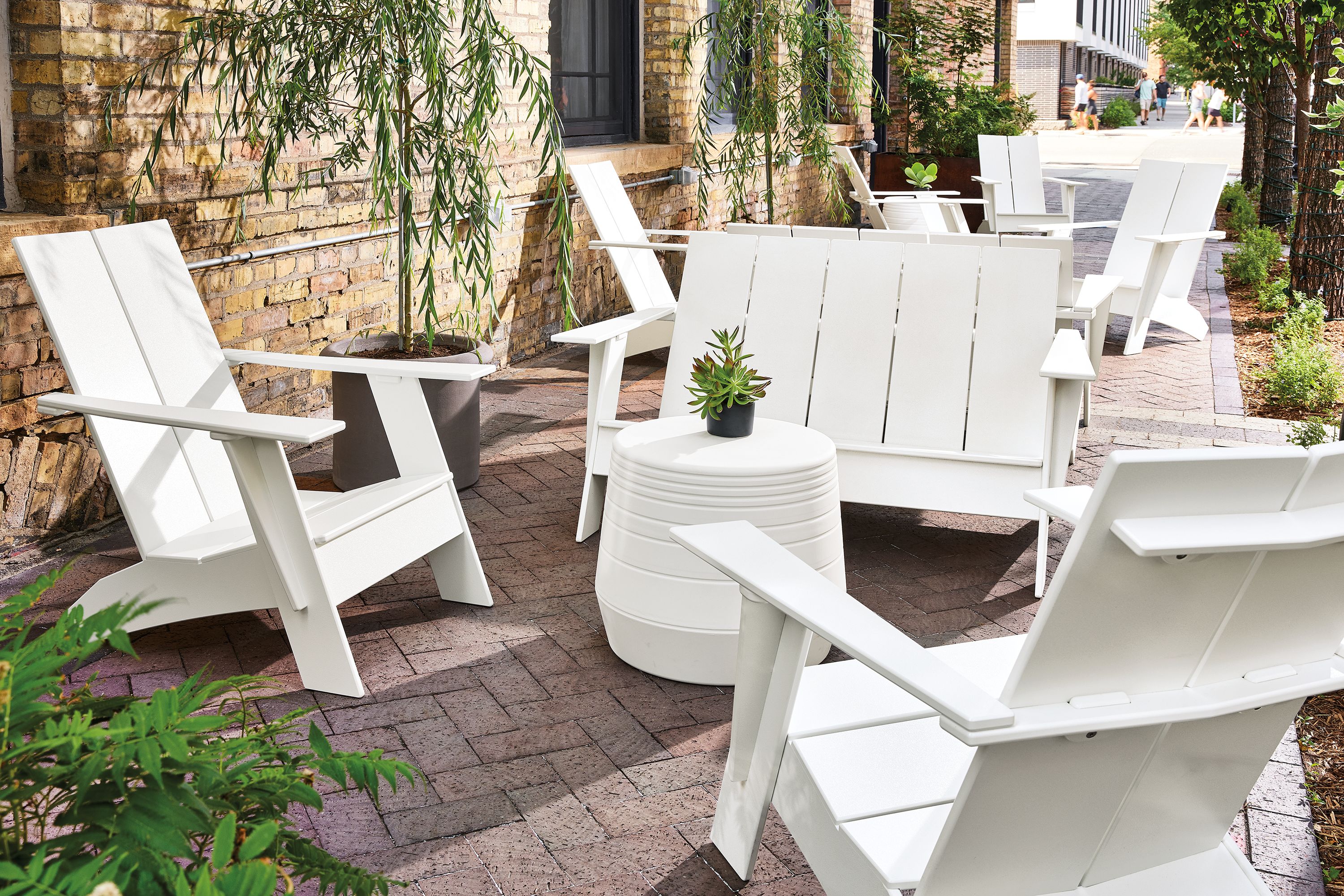 Outdoor brick walkway with several white emmet sofas and chairs and a cusp stool in white.