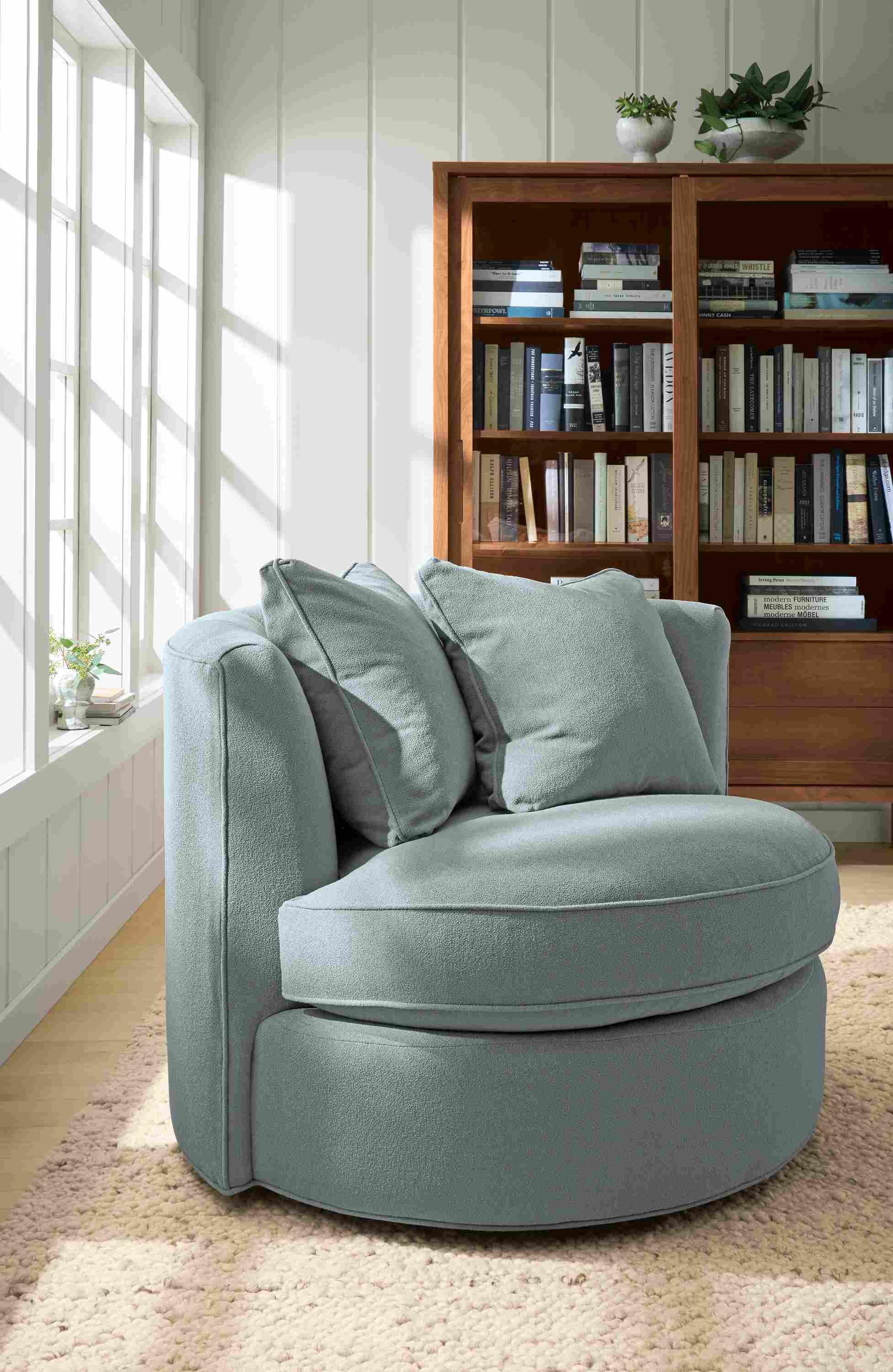 Living room with Eos swivel chair in Dusk Cadet, Emerson storage cabinet in walnut and Cobble rug in Ecru.
