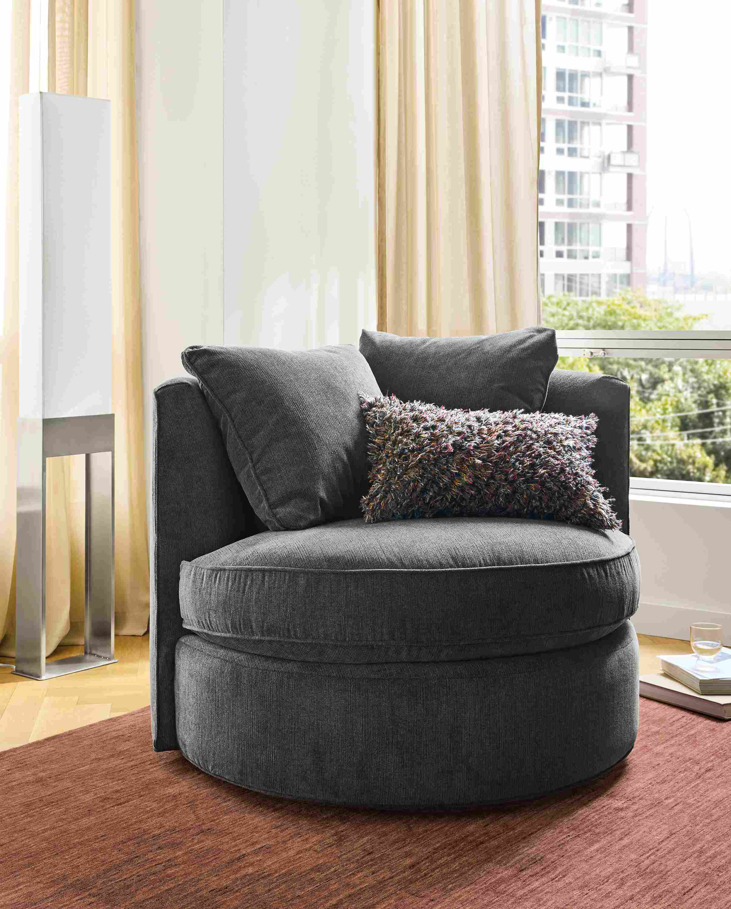 Living room with Eos swivel chair in Nigel Coal on a Nomad 8 by 10 rug in brick and  Iris floor lamp in stainless steel.