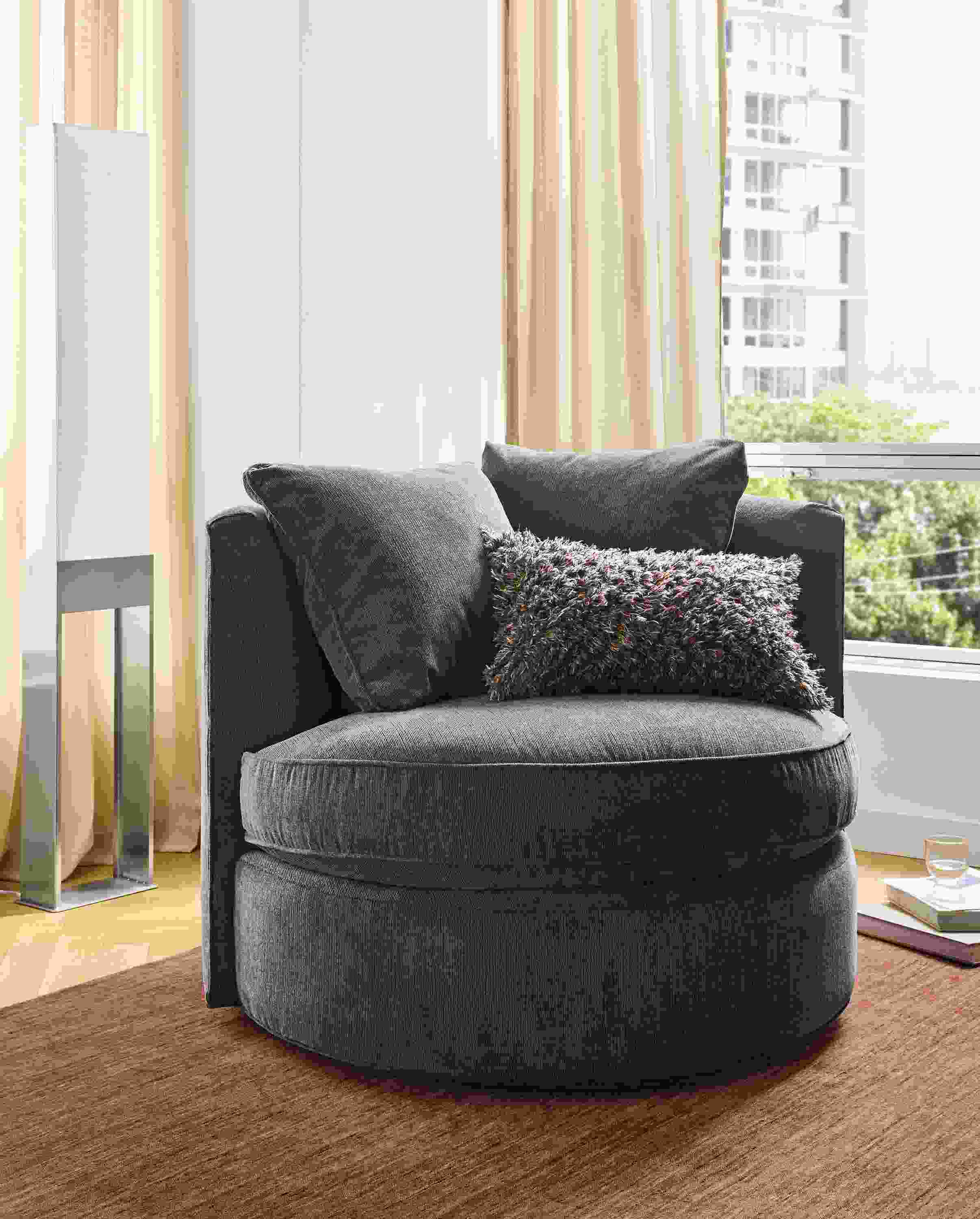 Living room with Eos swivel chair in Nigel Coal on a Nomad 8 by 10 rug in brick and  Iris floor lamp in stainless steel.