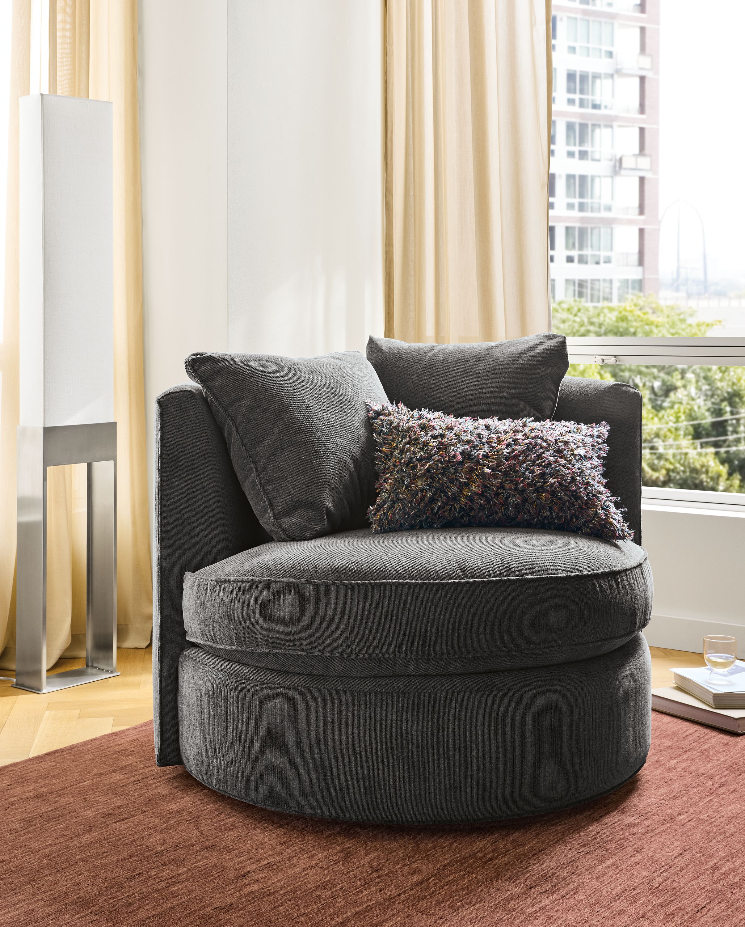 Living room with Eos swivel chair in Nigel Coal on a Nomad 8 by 10 rug in brick and  Iris floor lamp in stainless steel.