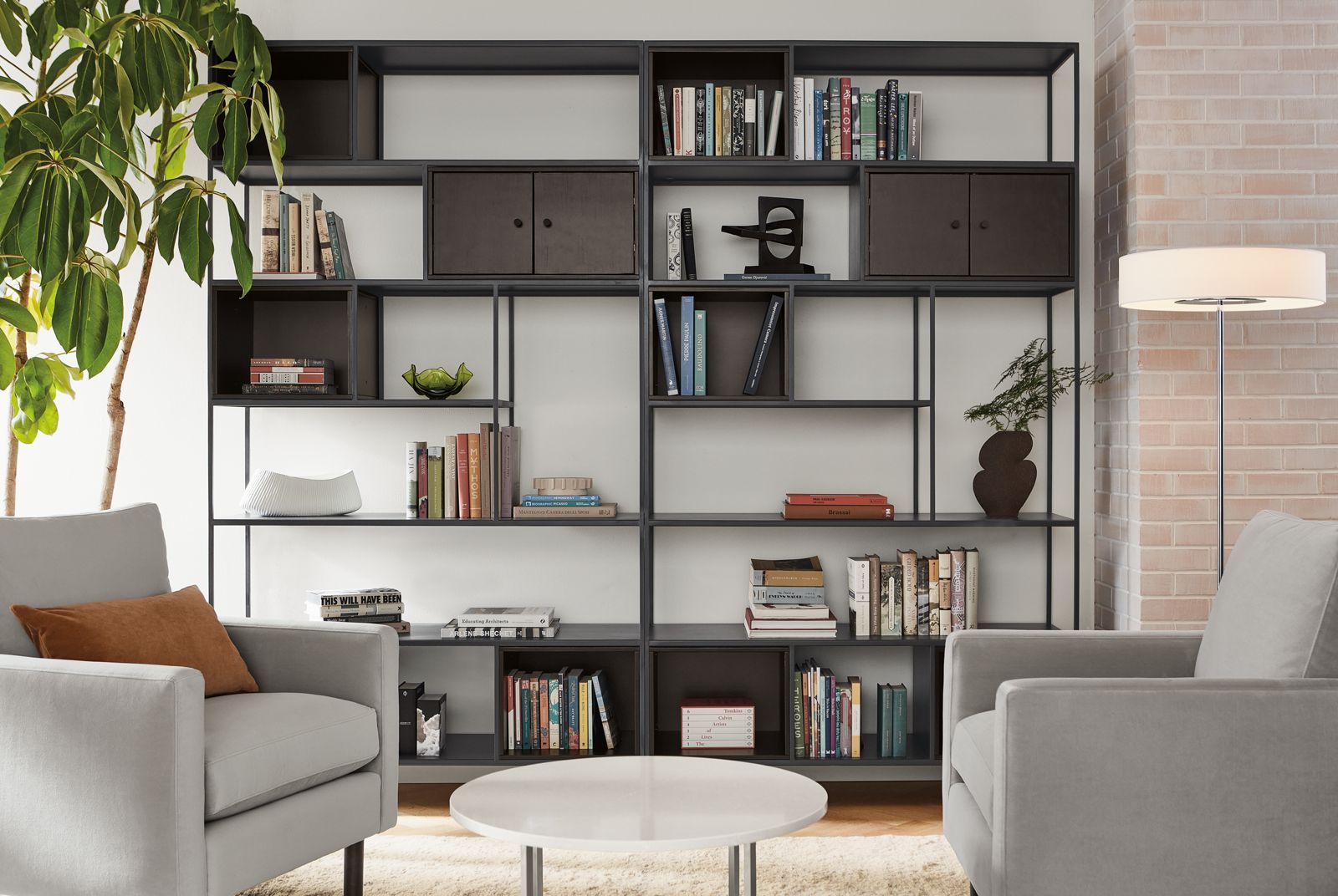 Living room setting with two Foshay 48-wide Bookcases in natural steel with charcoal Inserts, two Jasper 30-inch Chairs and Classic 27-Round Coffee Table.