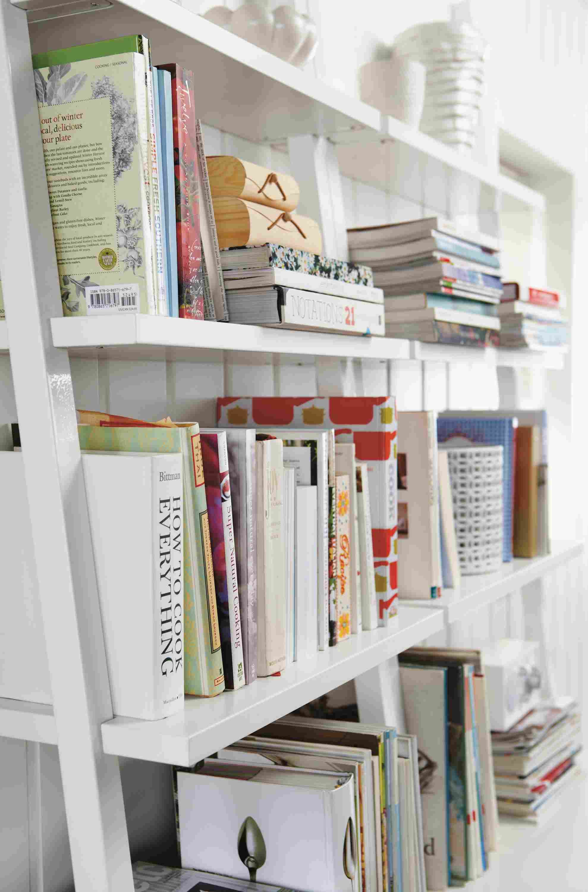 Living room with 2 Gallery leaning shelves in white filled with books.
