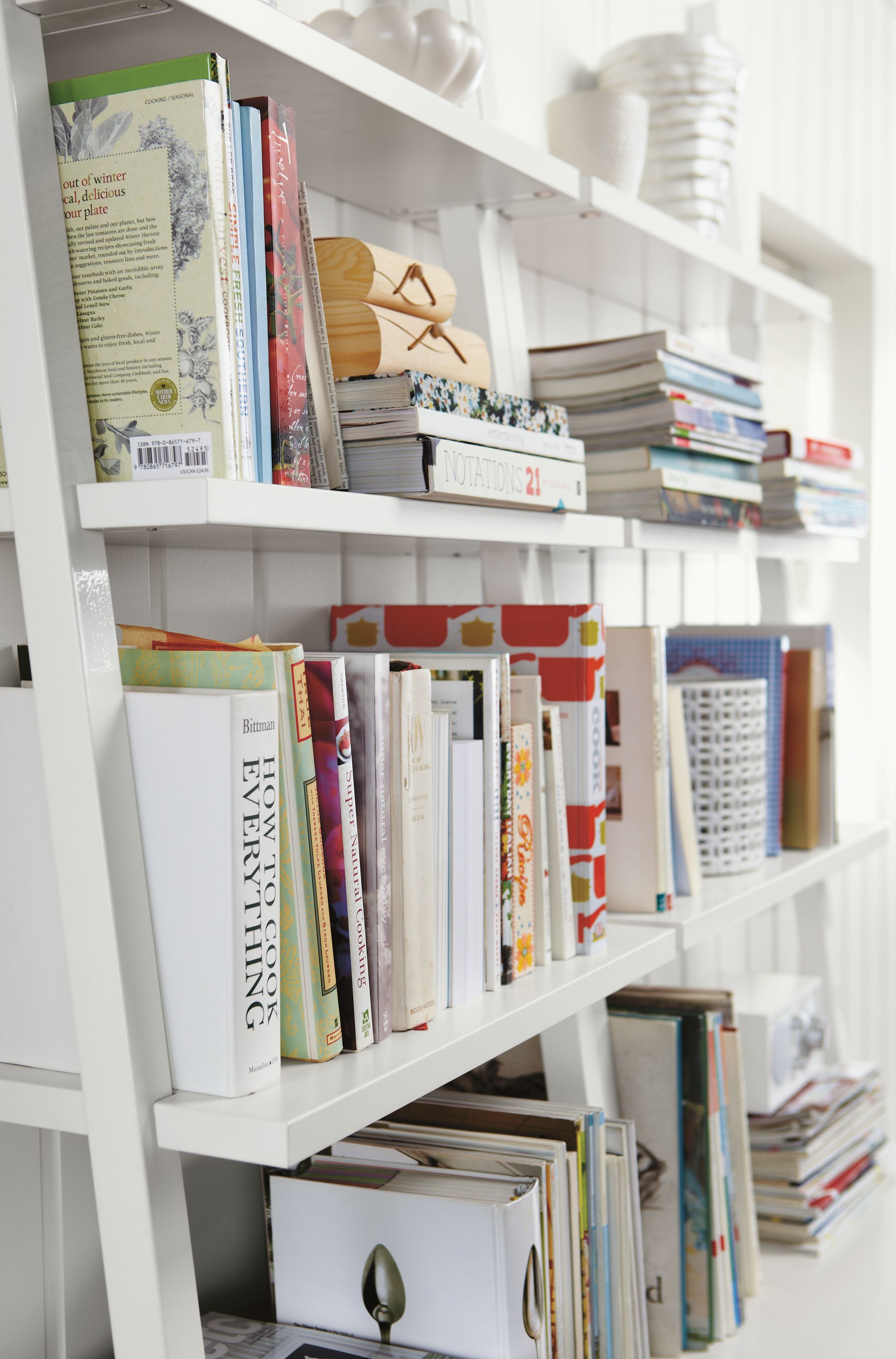 Living room with 2 Gallery leaning shelves in white filled with books.