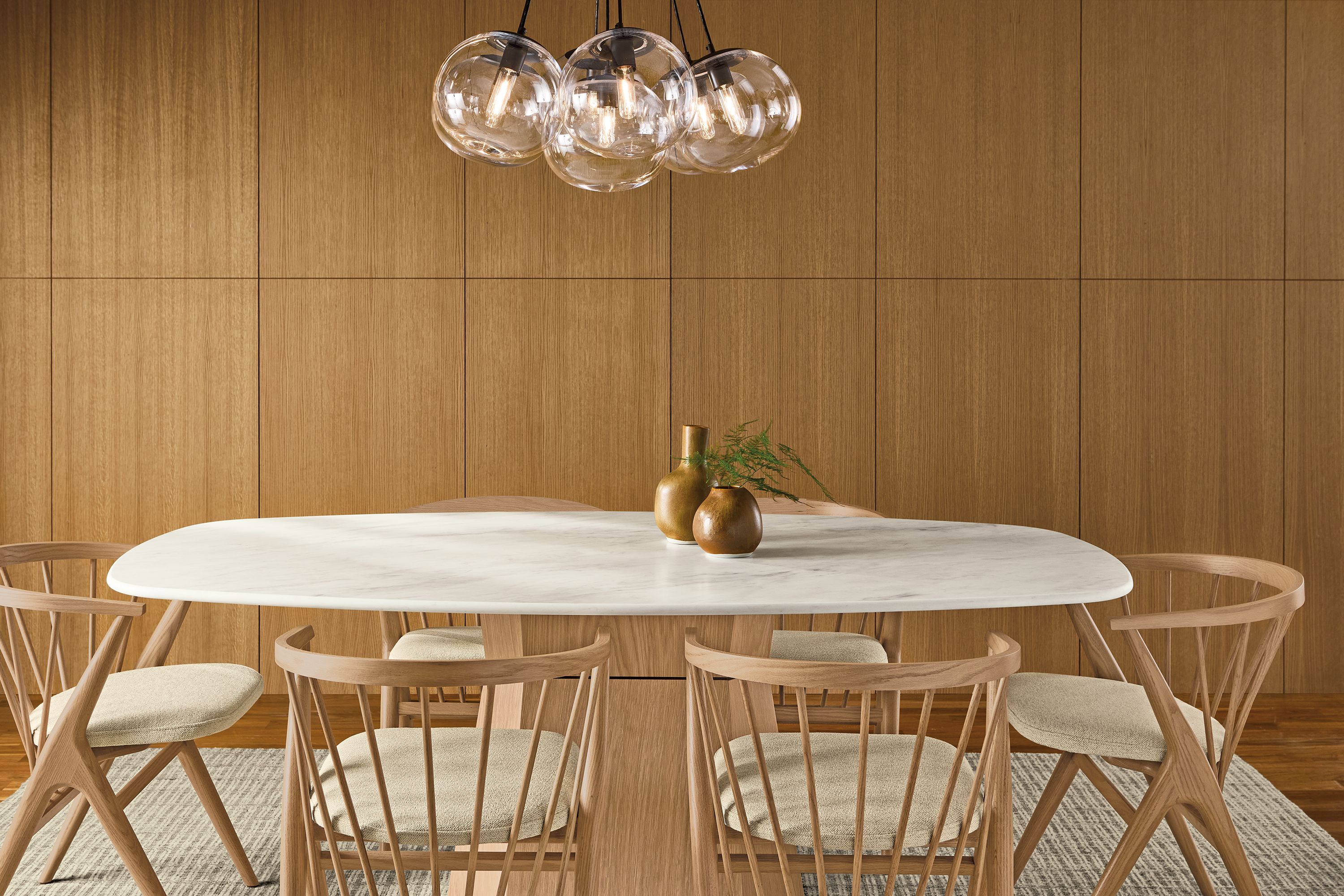Dining room with Glover 76-wide boat top table in rye on red oak with marbled warm white quartz and soren arm chairs in rye on red oak and tatum natural.