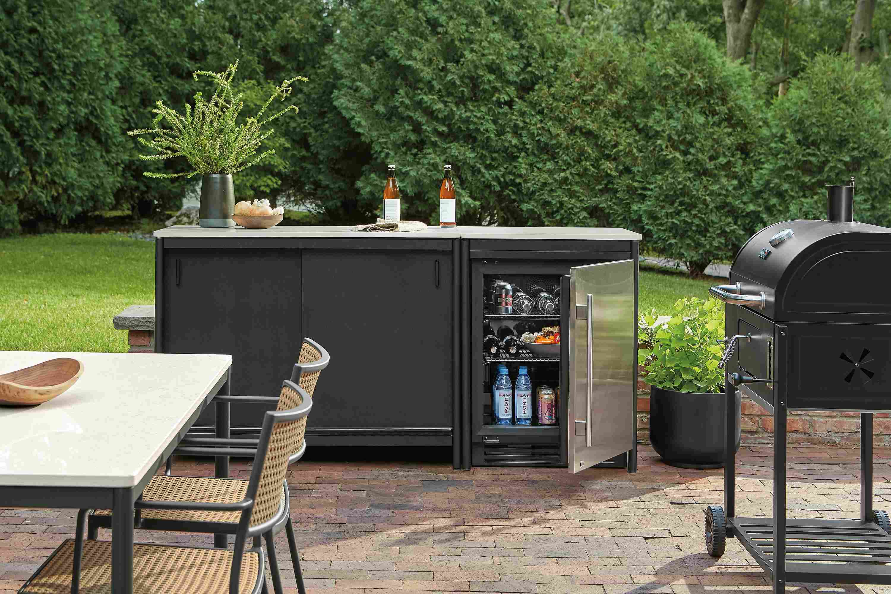 Outdoor space with Granger modular outdoor kitchen set in black with fridge with door open.