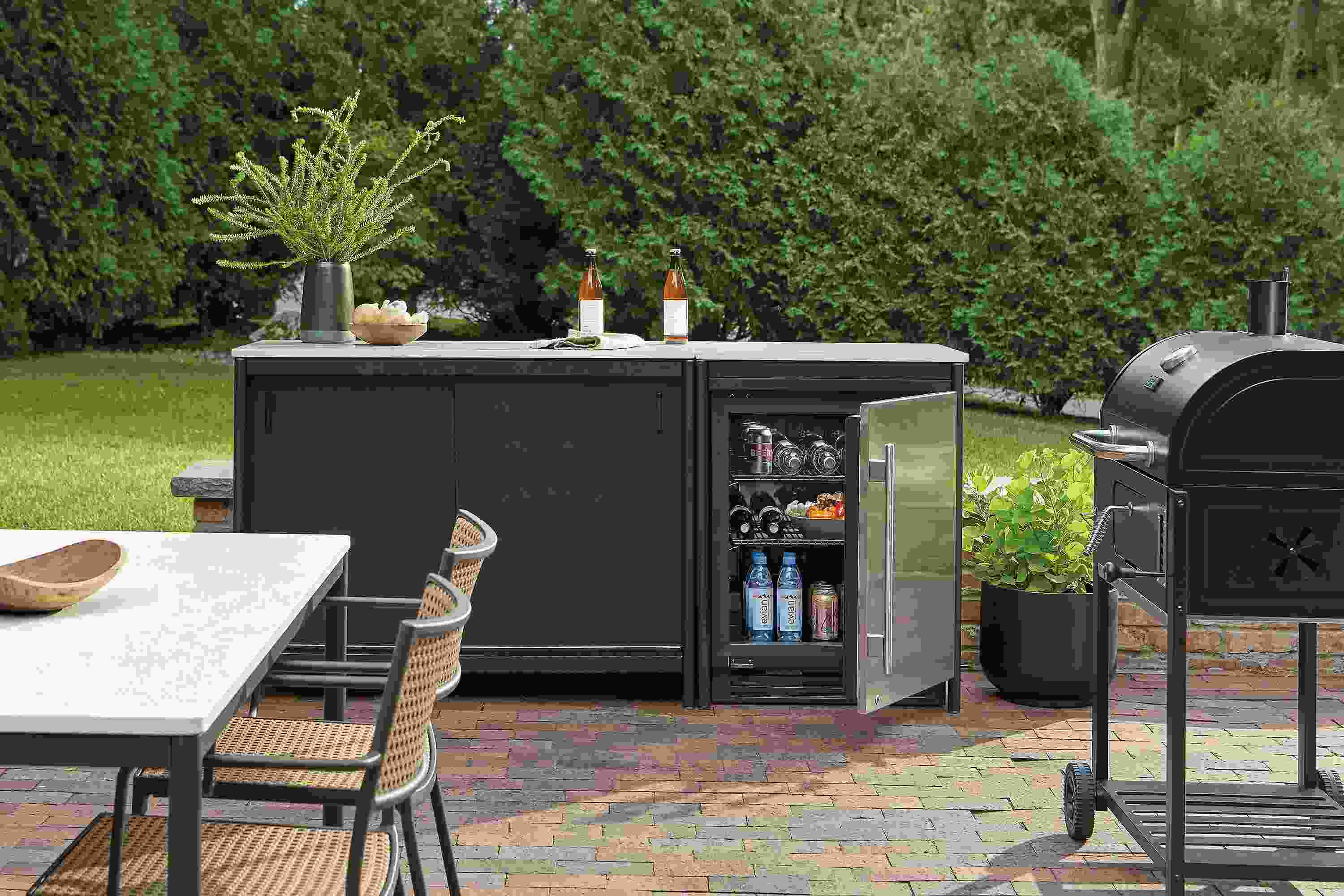 Outdoor space with Granger modular outdoor kitchen set in black with fridge with door open.