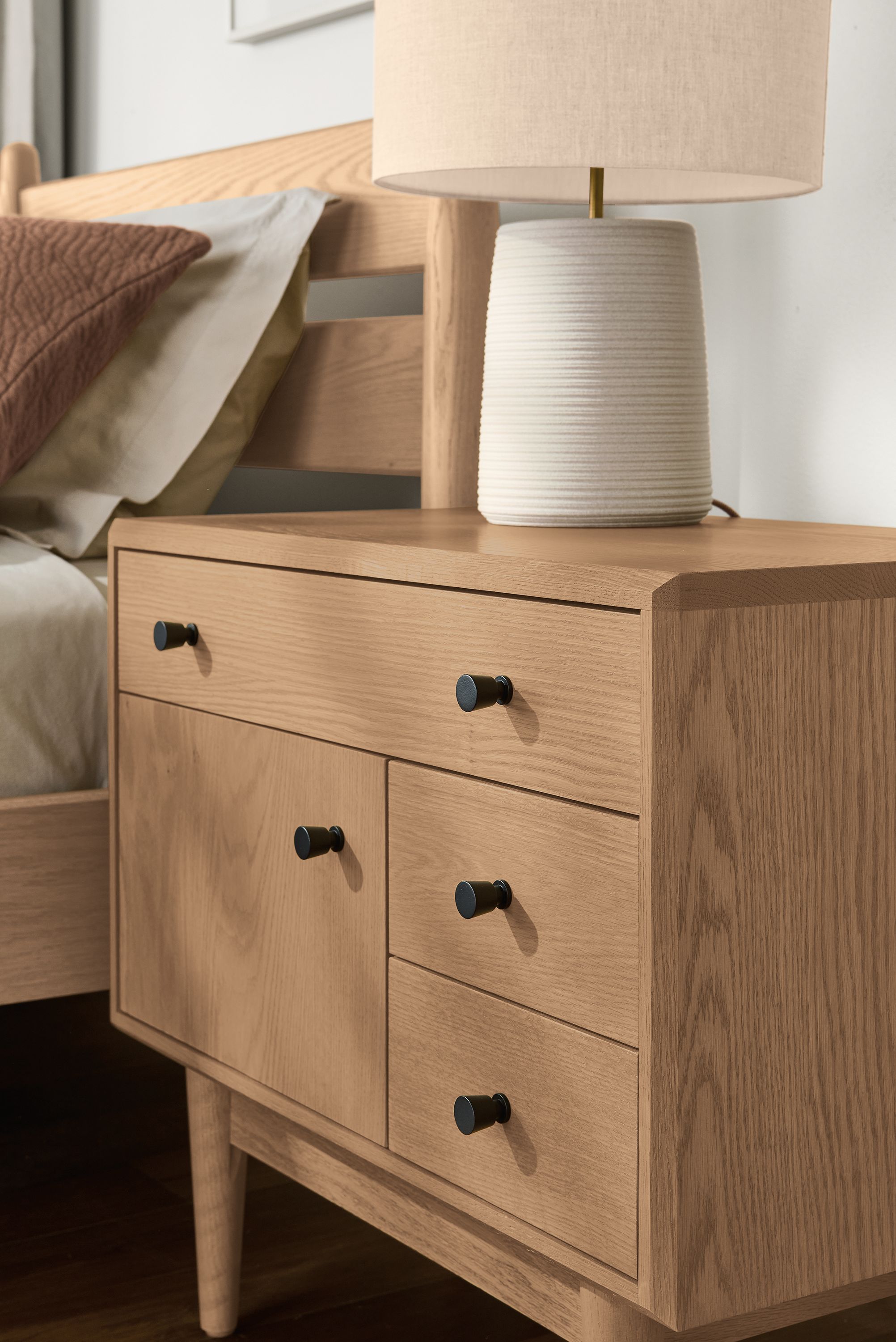 Detail of a Grove 1-door, 3-drawer nightstand in rye on red oak and Bruin table lamp in bone.