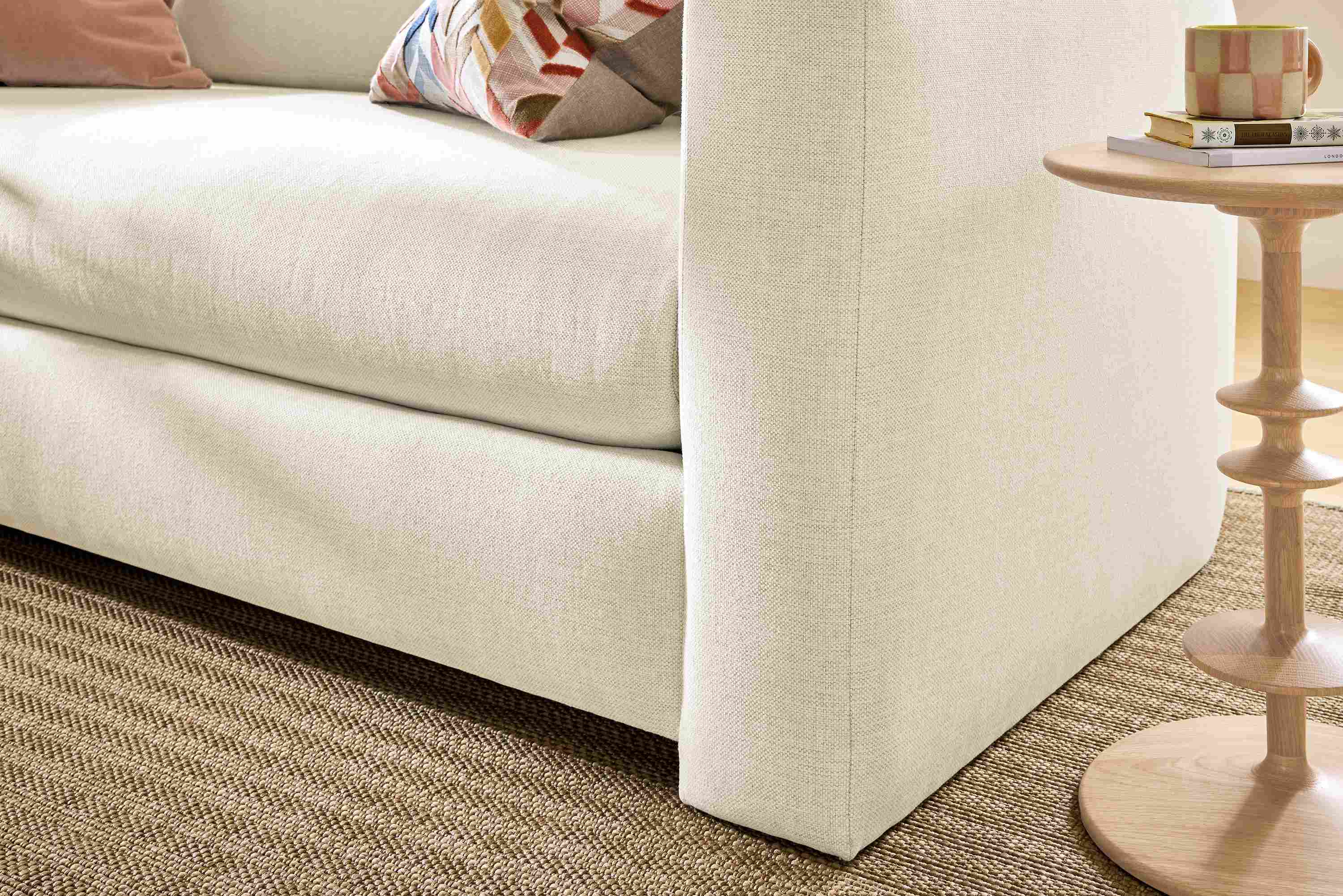 Detail of the front corner of a Hannah 76-wide bench cushion sofa in sumner ivory and Leland rug in sand in a living room.