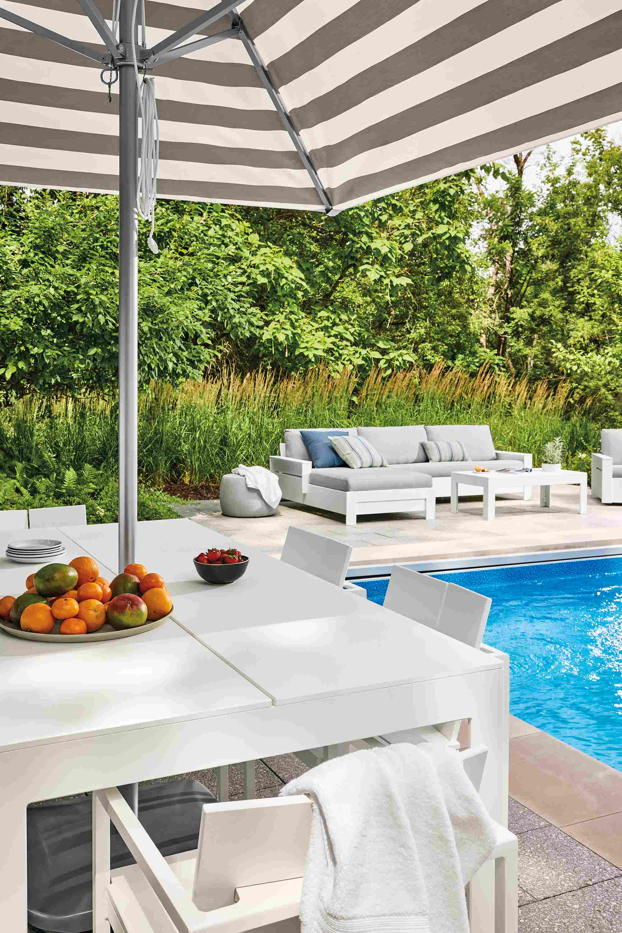 Poolside area with Henry 80-wide table and 6 Mattix arm chairs in white HDPE and Pacifica Umbrella in Jace stripe putty.