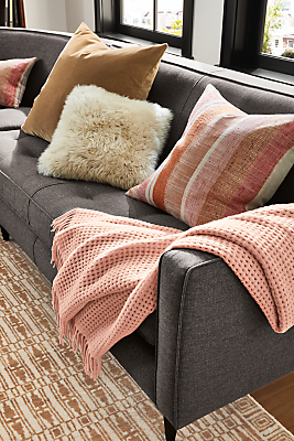 detail of homage throw blanket in blush draped over gray sofa.