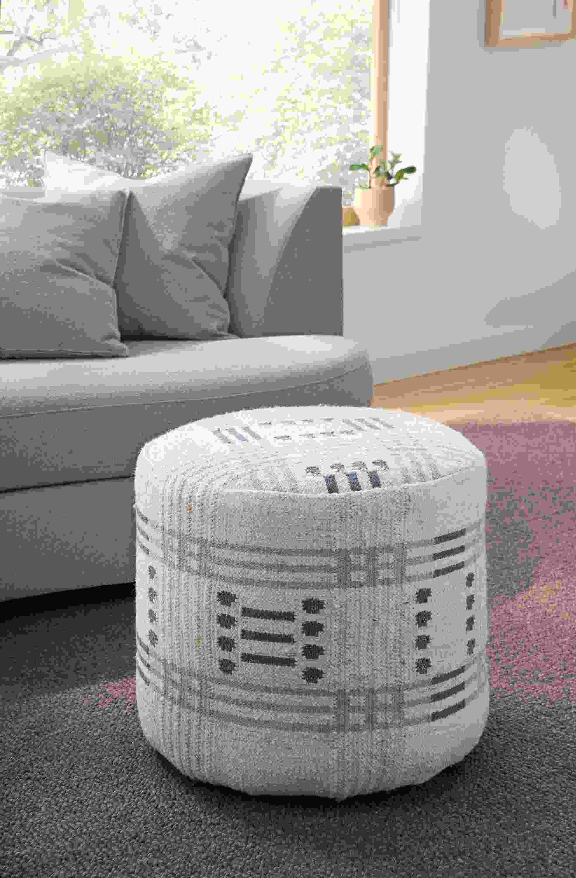 Living room with detail of Idira 20-diameter ottoman in Misha Grey and Arden low-loop 8 by 10 rug in Earth.