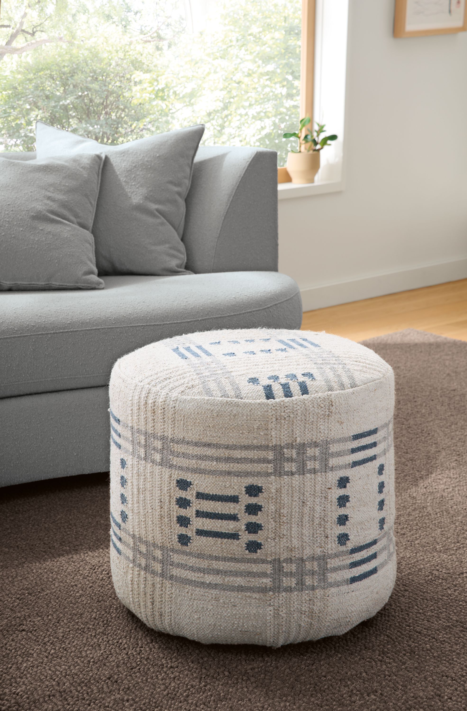 Living room with detail of Idira 20-diameter ottoman in Misha Grey and Arden low-loop 8 by 10 rug in Earth.