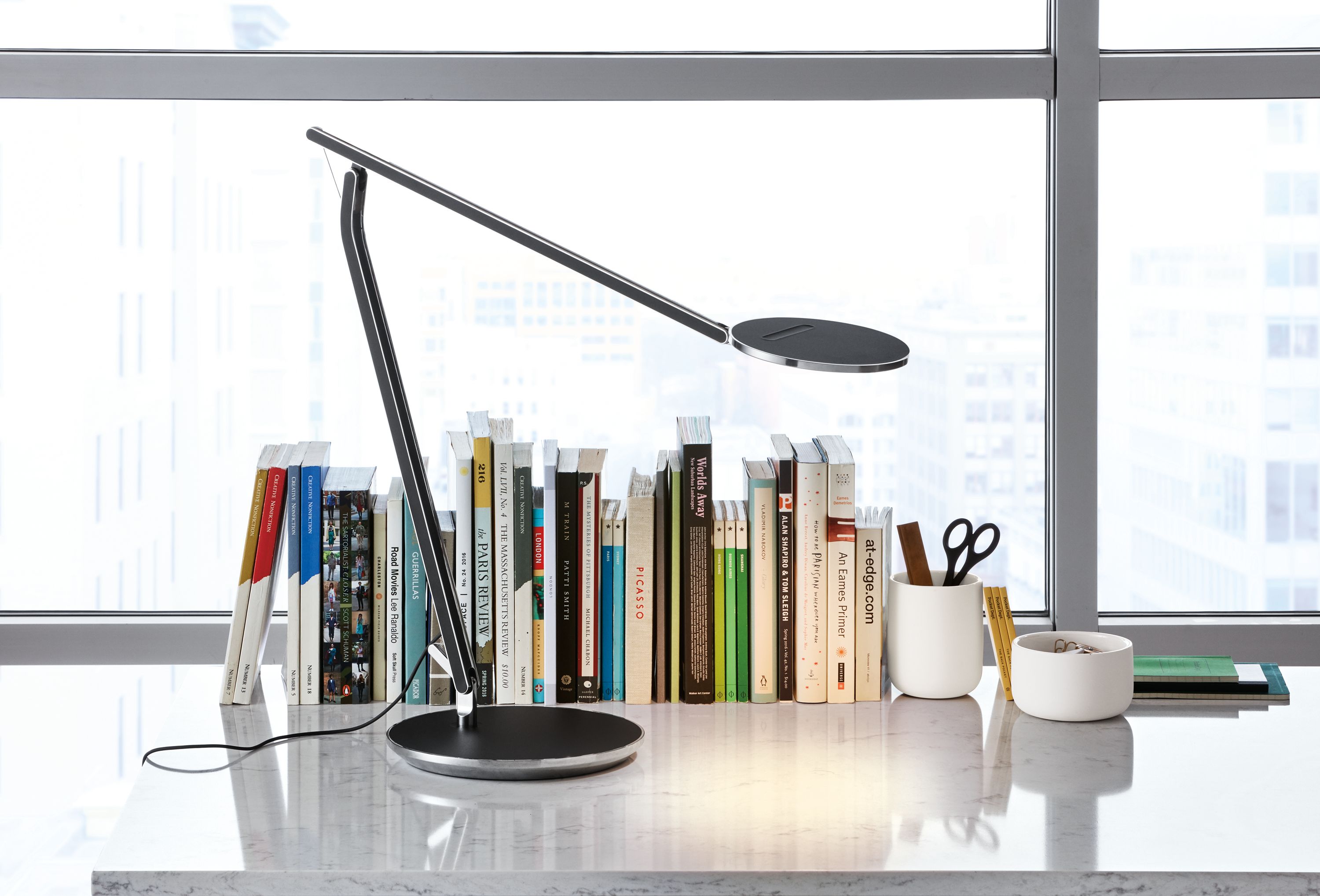 Detail of Infinity task lamp on a desk near a window.