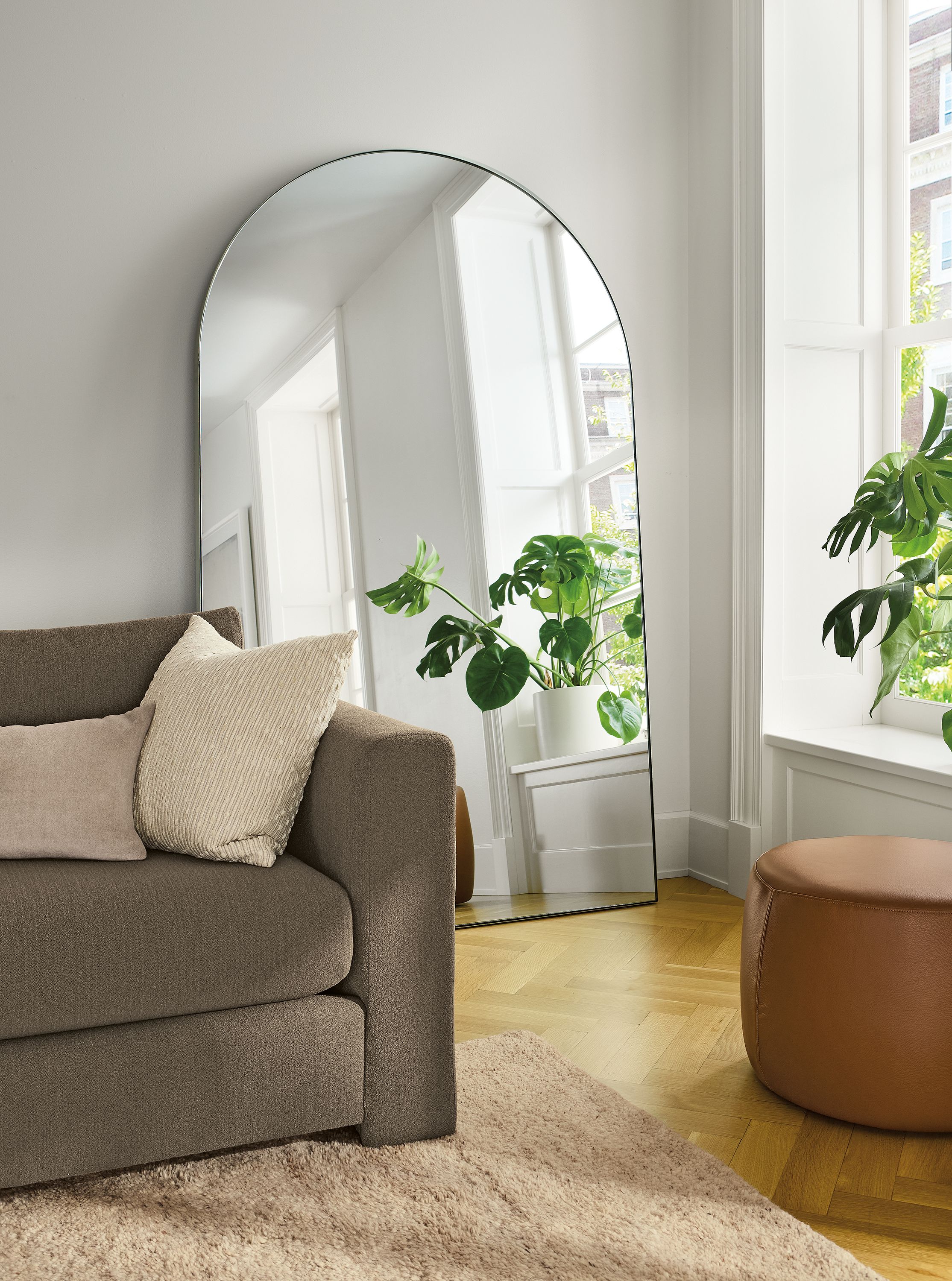 Living room with Infinity 48-wide arched floor mirror in stainless steel and Hannah sofa in dusk mink.