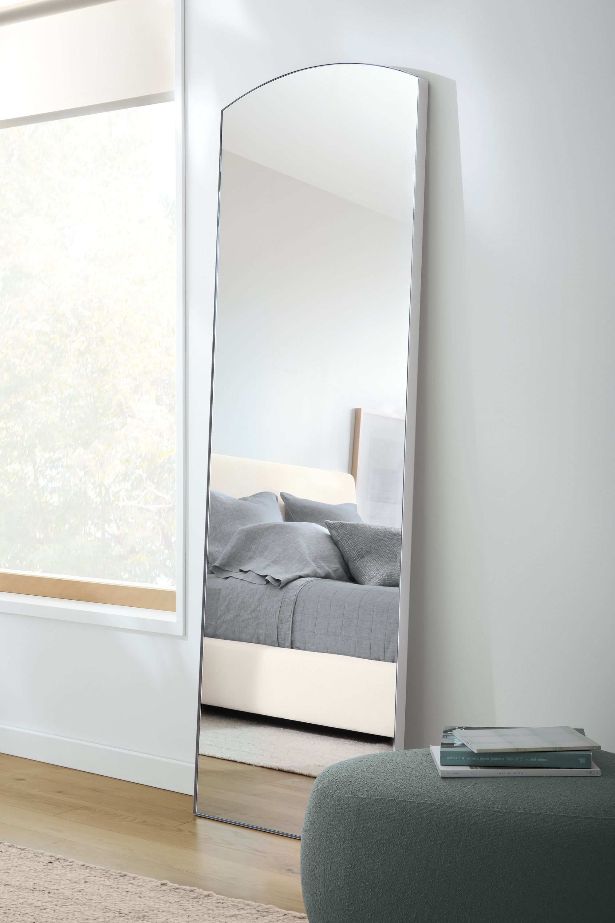 Bedroom with an Infinity 26 by 80 arched floor mirrow in stainless steel and an Asher ottoman in Declan Haze.