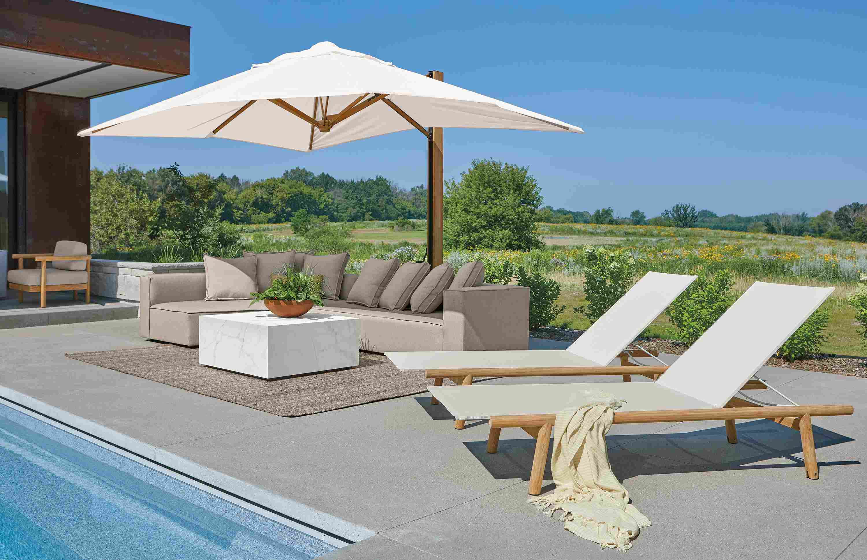Poolside area with 2 Isley chaises in teak with salt sling and Banda cantilever patio umbrella in teak and halo white.
