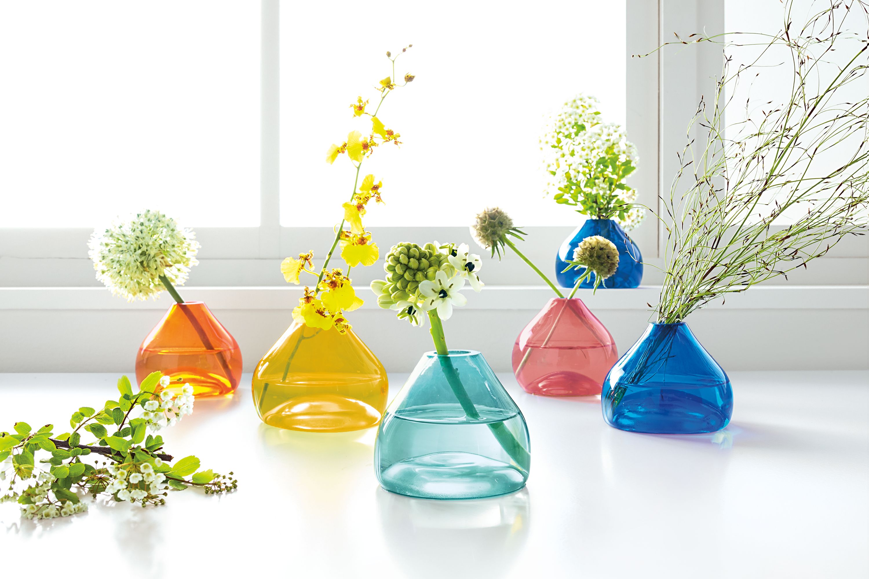 detail of jewel bud vases in various colors holding flowers displayed on counter.