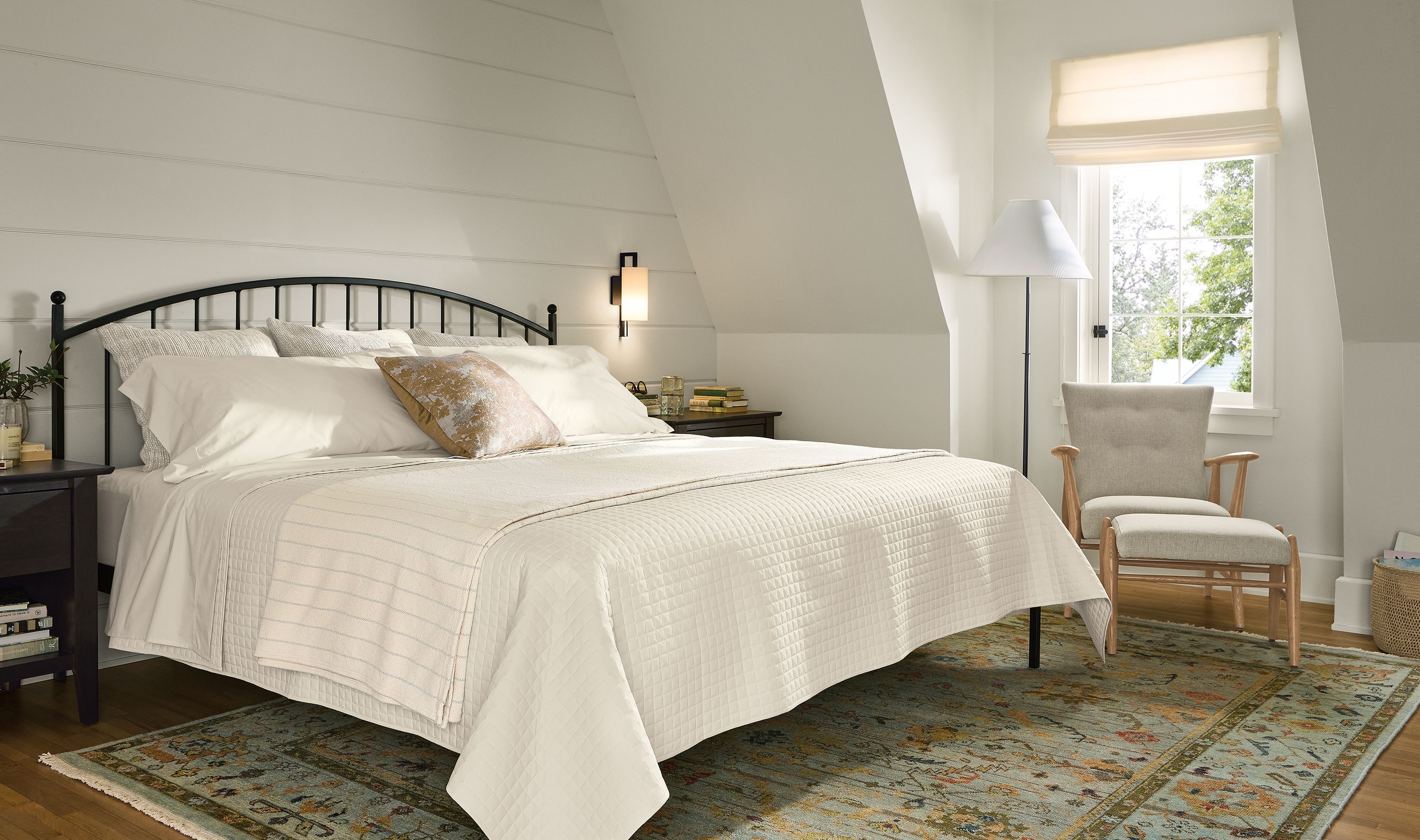 Bedroom with a Joyce king bed in natural steel with a Jonas lounge chair and ottoman in sumner lined and sundar rug in sky.