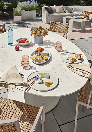 Closeup of Julian outdoor oval table with four Plat chairs in natural with rose frame.