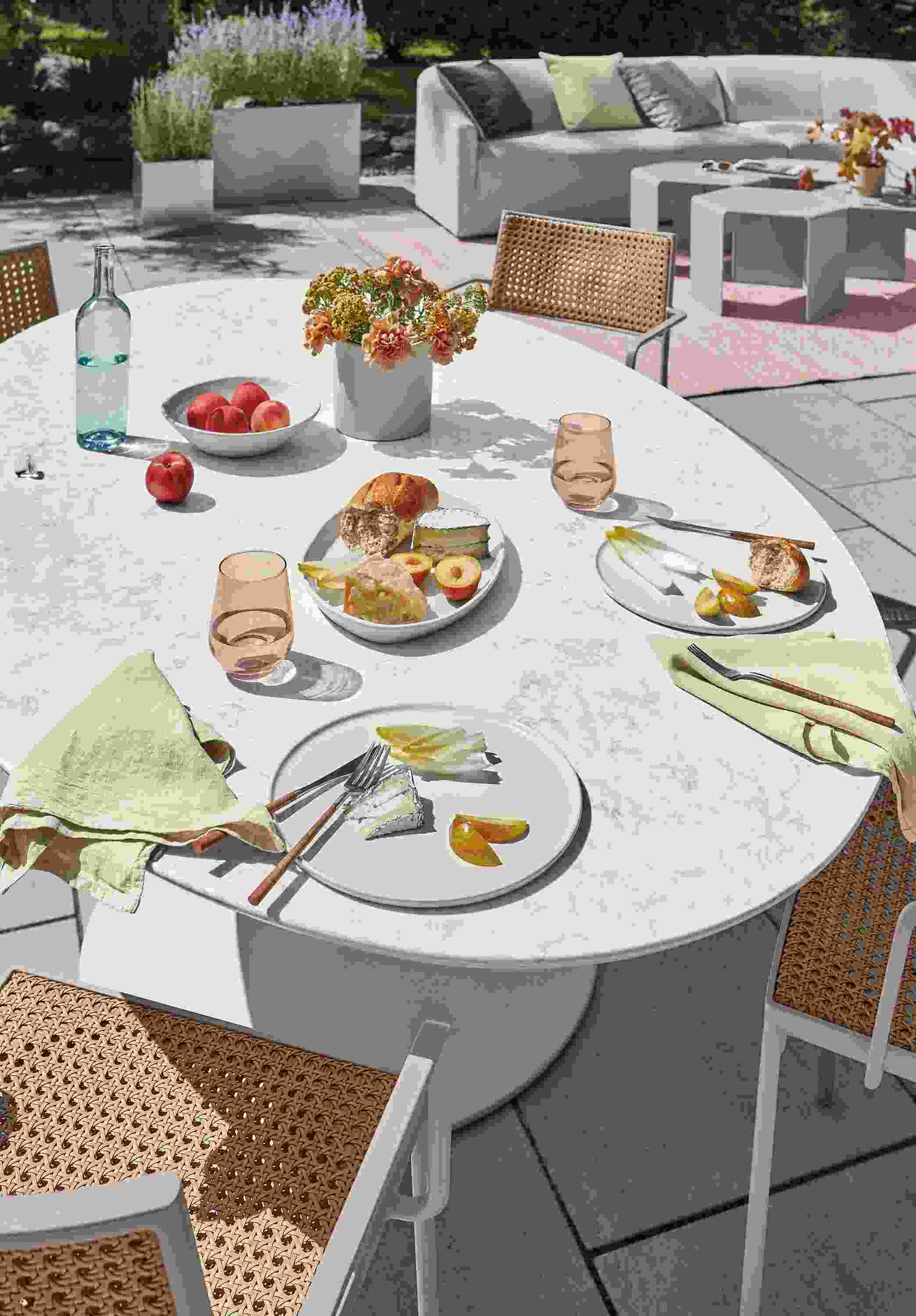 Closeup of Julian outdoor oval table with four Plat chairs in natural with rose frame.