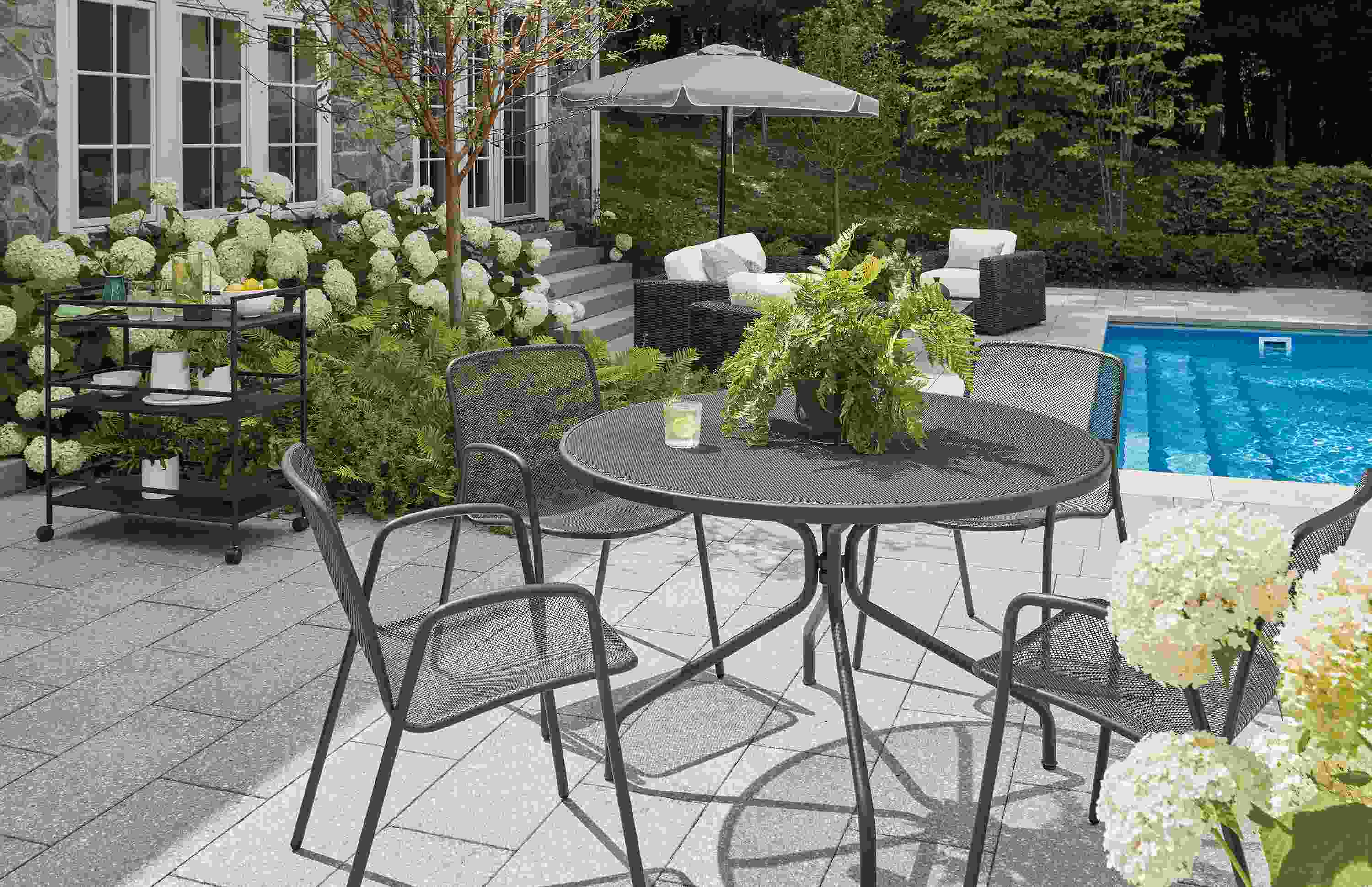 Pool patio with Kona round table and 4 Aruba chairs in graphite and Pacifica umbrella in Jace cement.