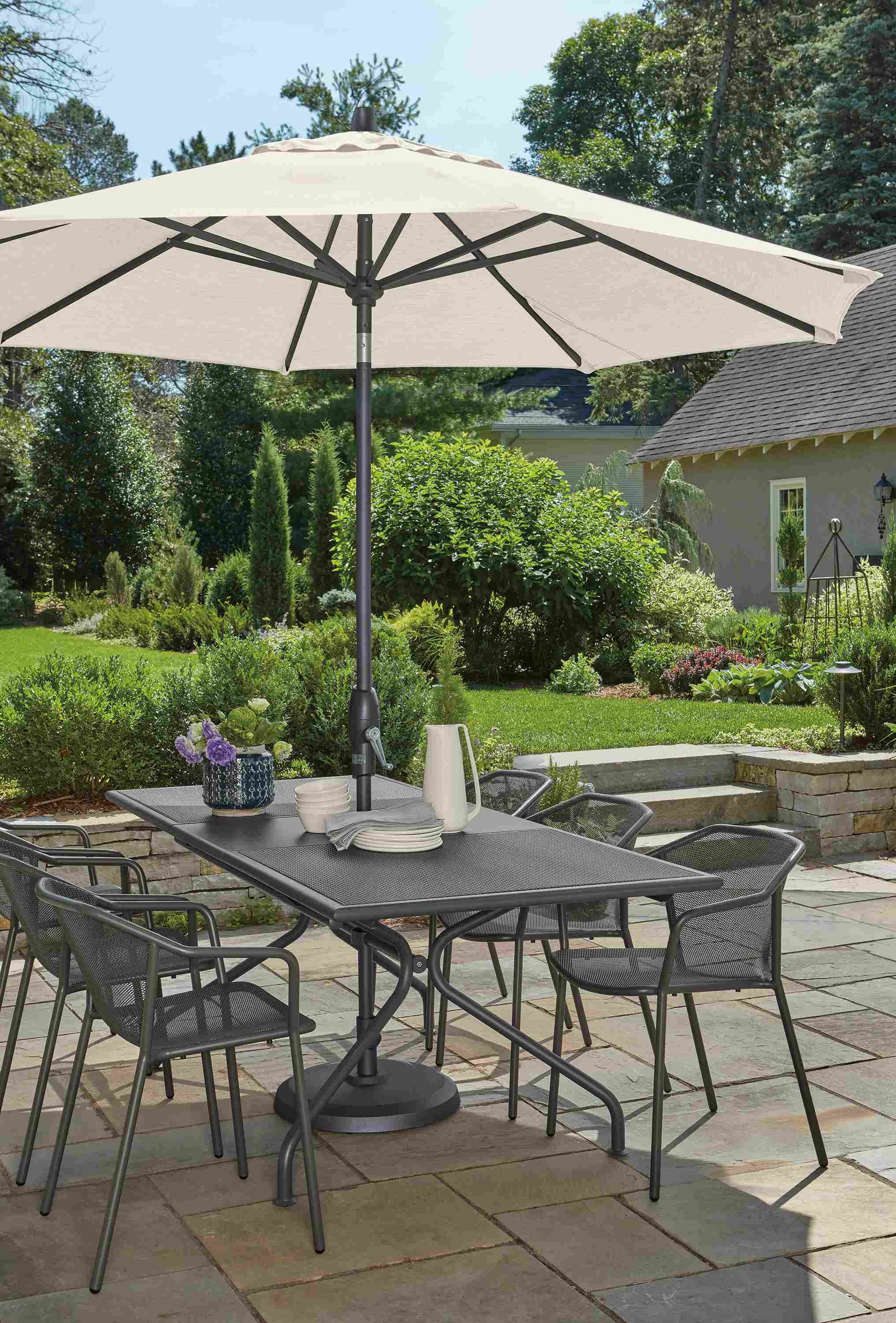 Outdoor patio with Kona extension table and six Theo chairs in graphite and Oahu umbrella in Tavros White.