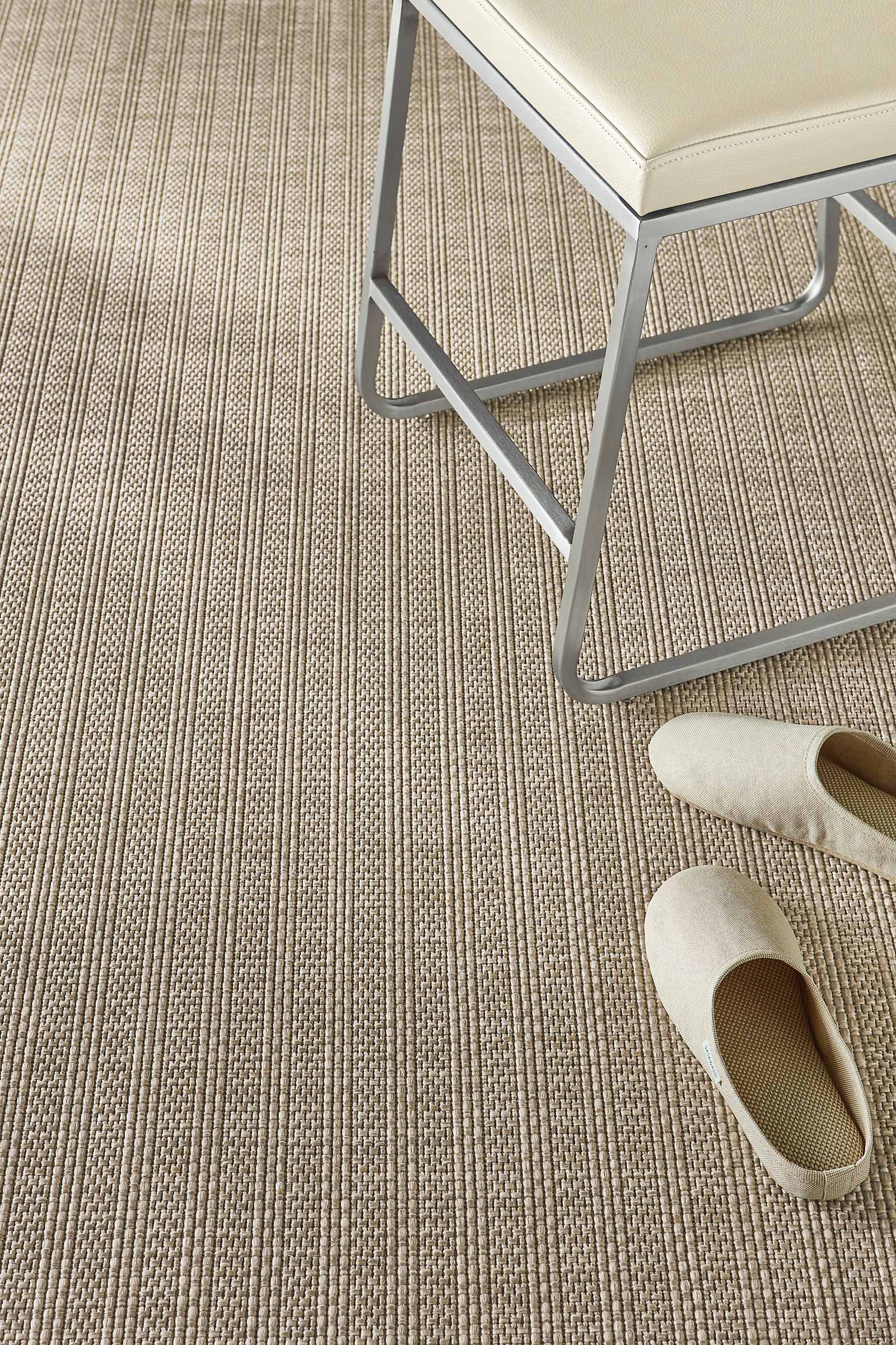 Detail shot showing partial Leland 8 by 10 rug in Cement and Collins low stool in Pesaro black leather.
