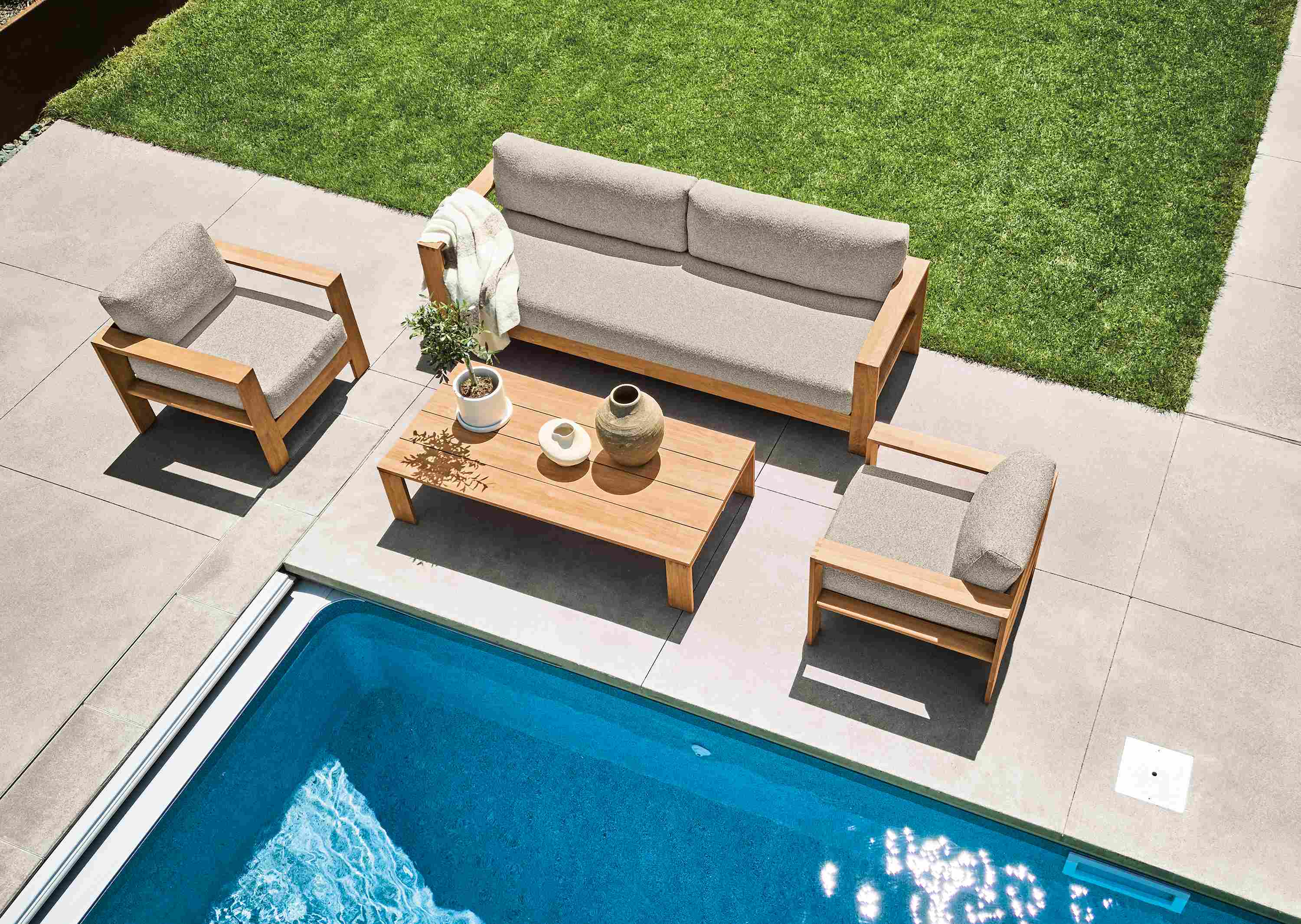 Overhead view of pool patio with Leti sofa, lounge chair and coffee table in teak heartwood and Kloss Otter.