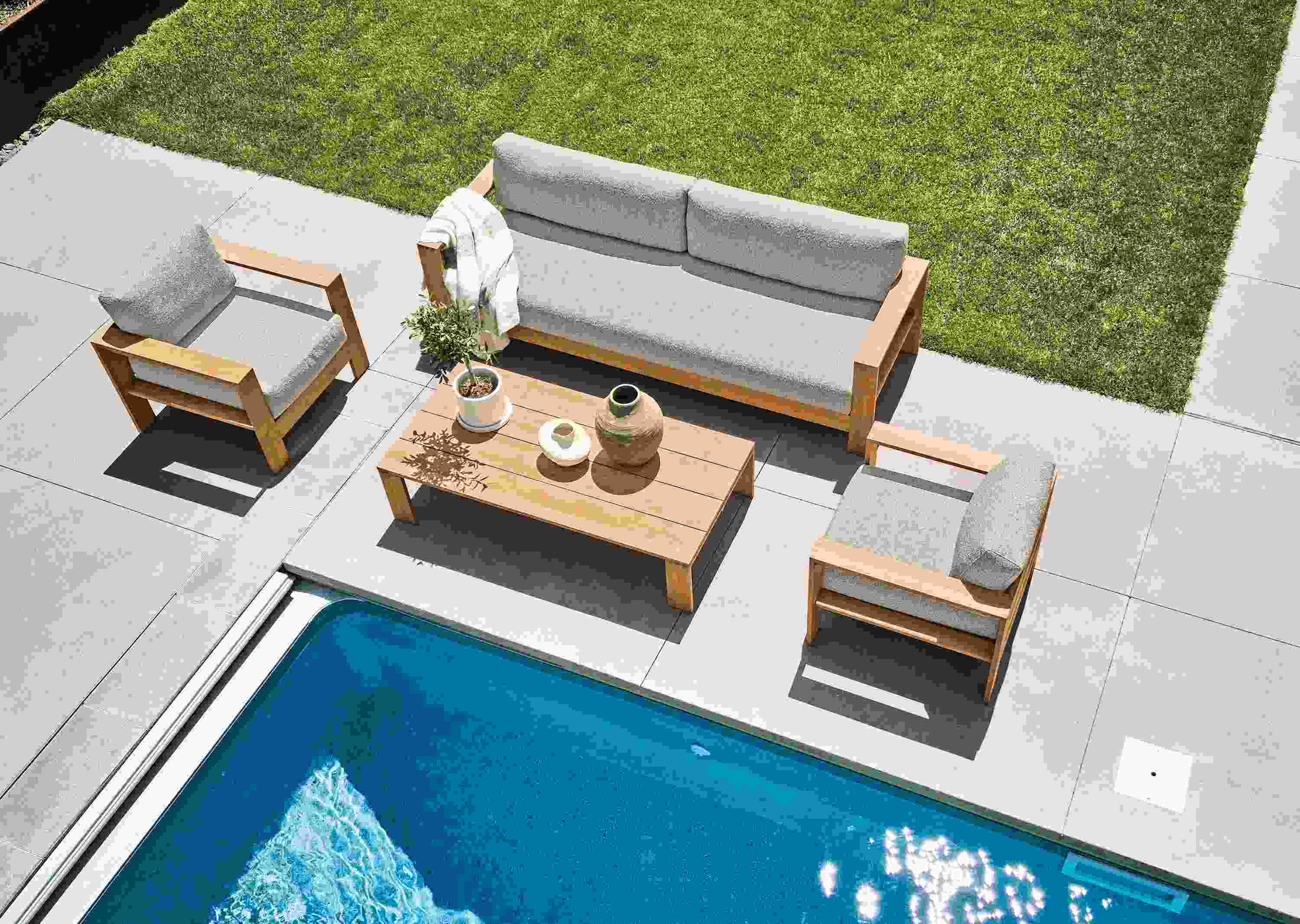 Overhead view of pool patio with Leti sofa, lounge chair and coffee table in teak heartwood and Kloss Otter.