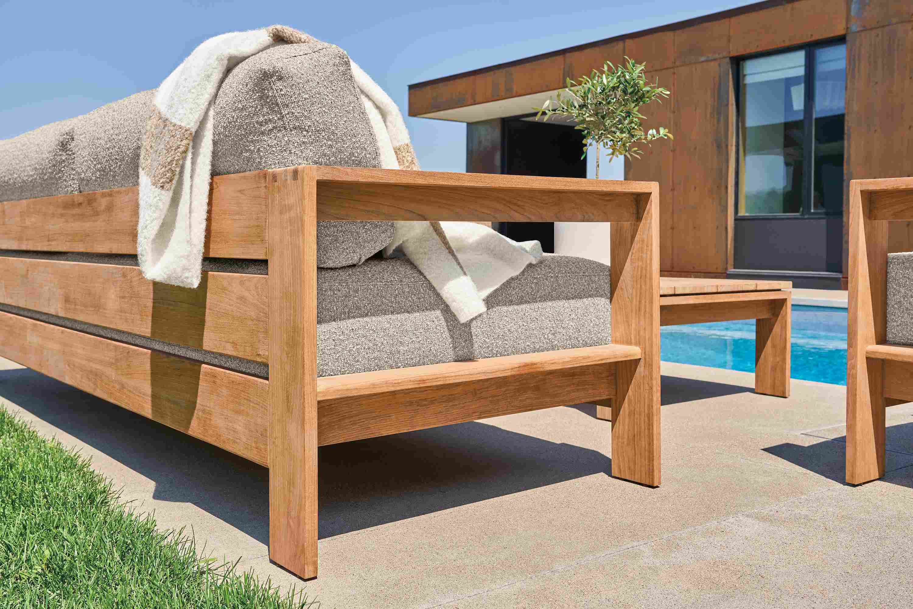 Low-angle detail of Leti sofa in teak heartwood and Kloss Otter on a pool patio.